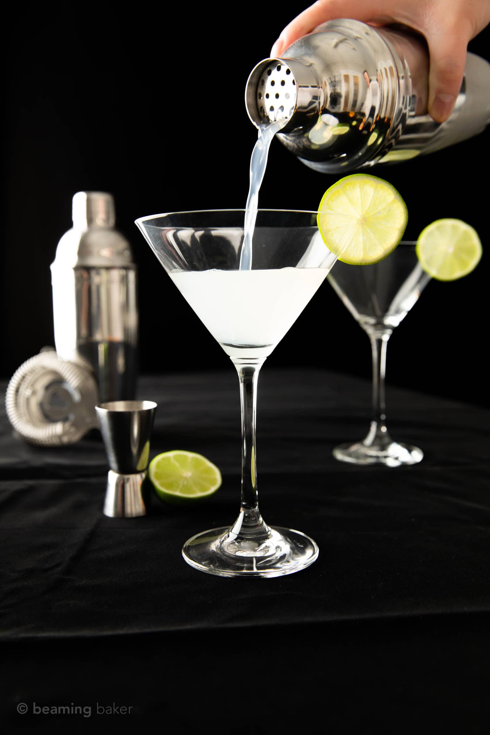 Straining gin gimlet from a stainless steel cocktail shaker into a martini glass