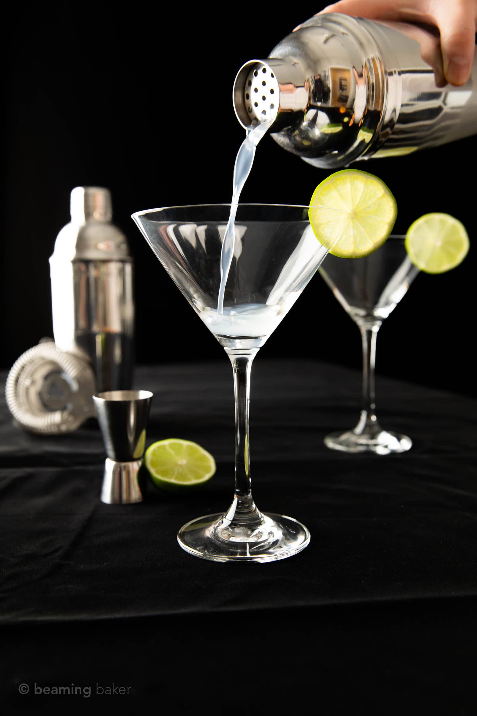 Just starting to pour gimlet into a martini glass garnished with a lime wedge