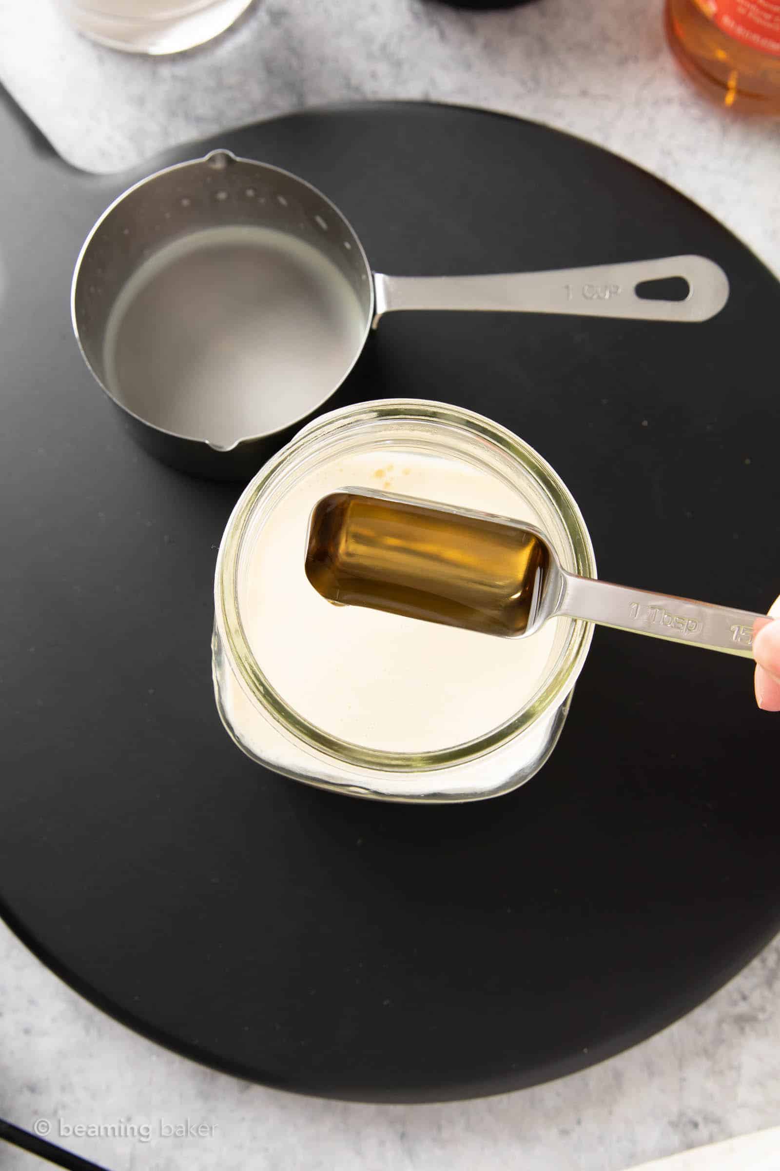 Metal one-tablespoon filled with apple cider vinegar dropping into a jar filled with soy milk to make vegan buttermilk