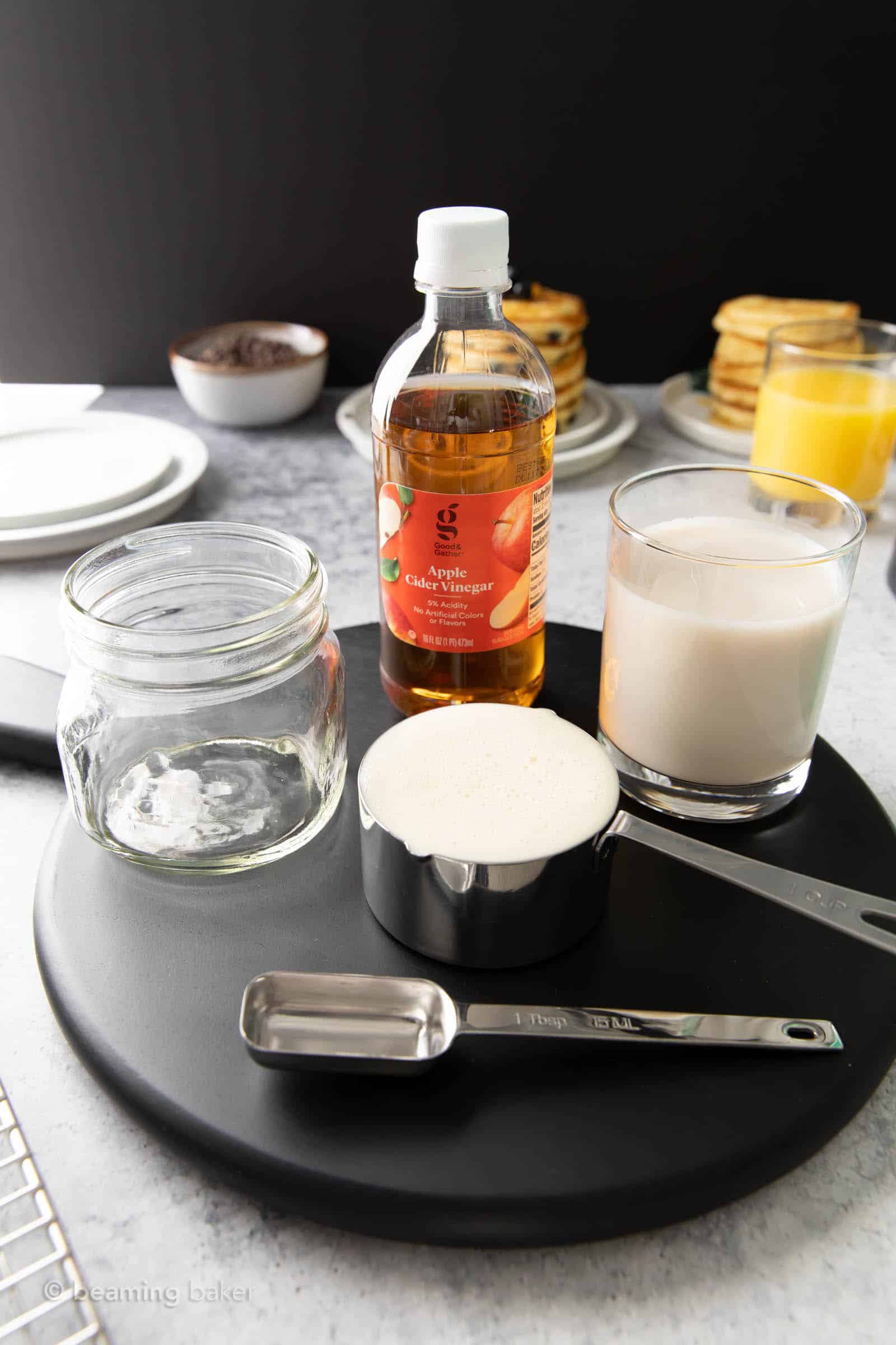 vegan buttermilk ingredients laid out on a black serving board, including apple cider vinegar and soy milk