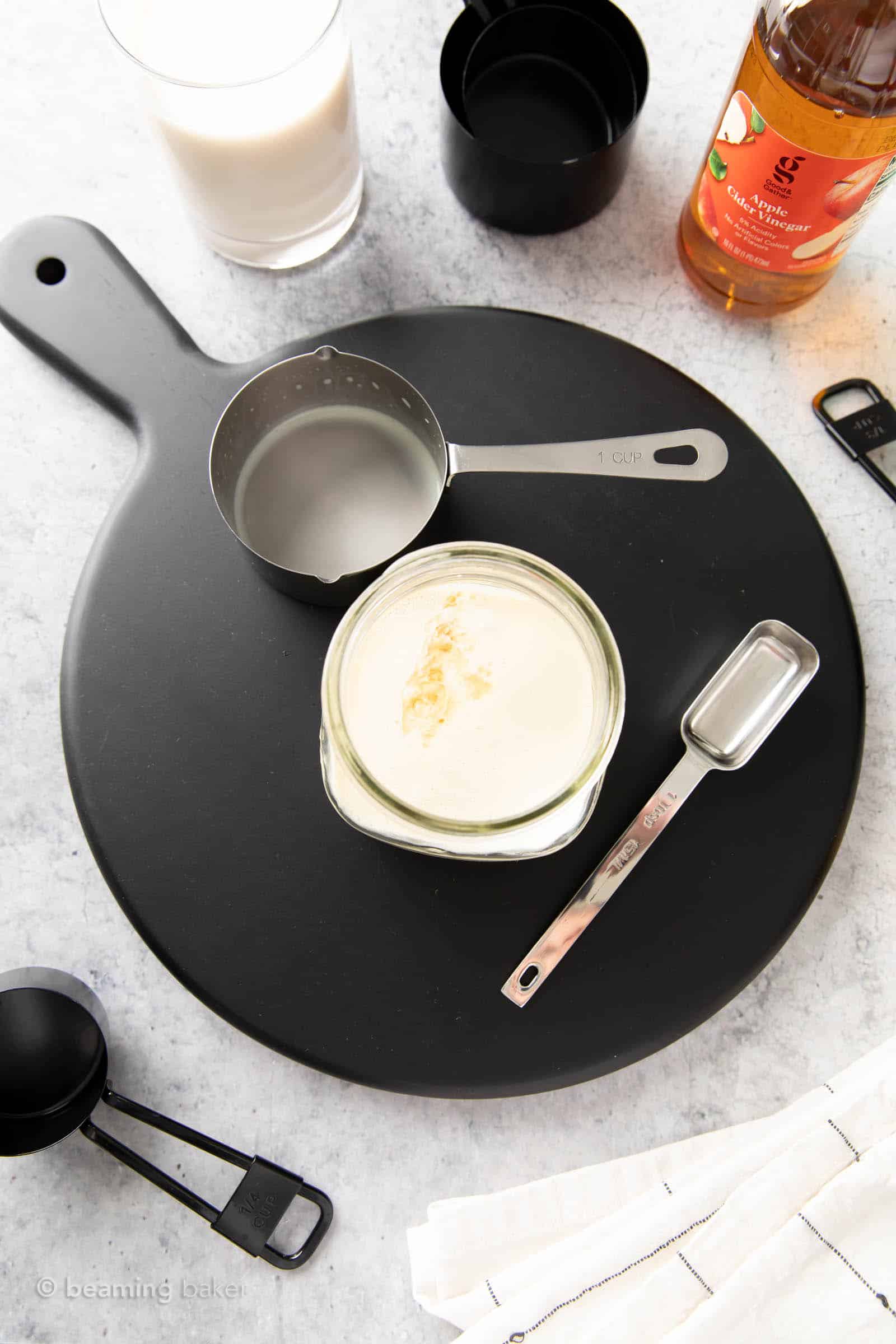 overhead shot of the entire tablespoon of apple cider vinegar sitting in a glass of soy milk with two measuring tools nearby