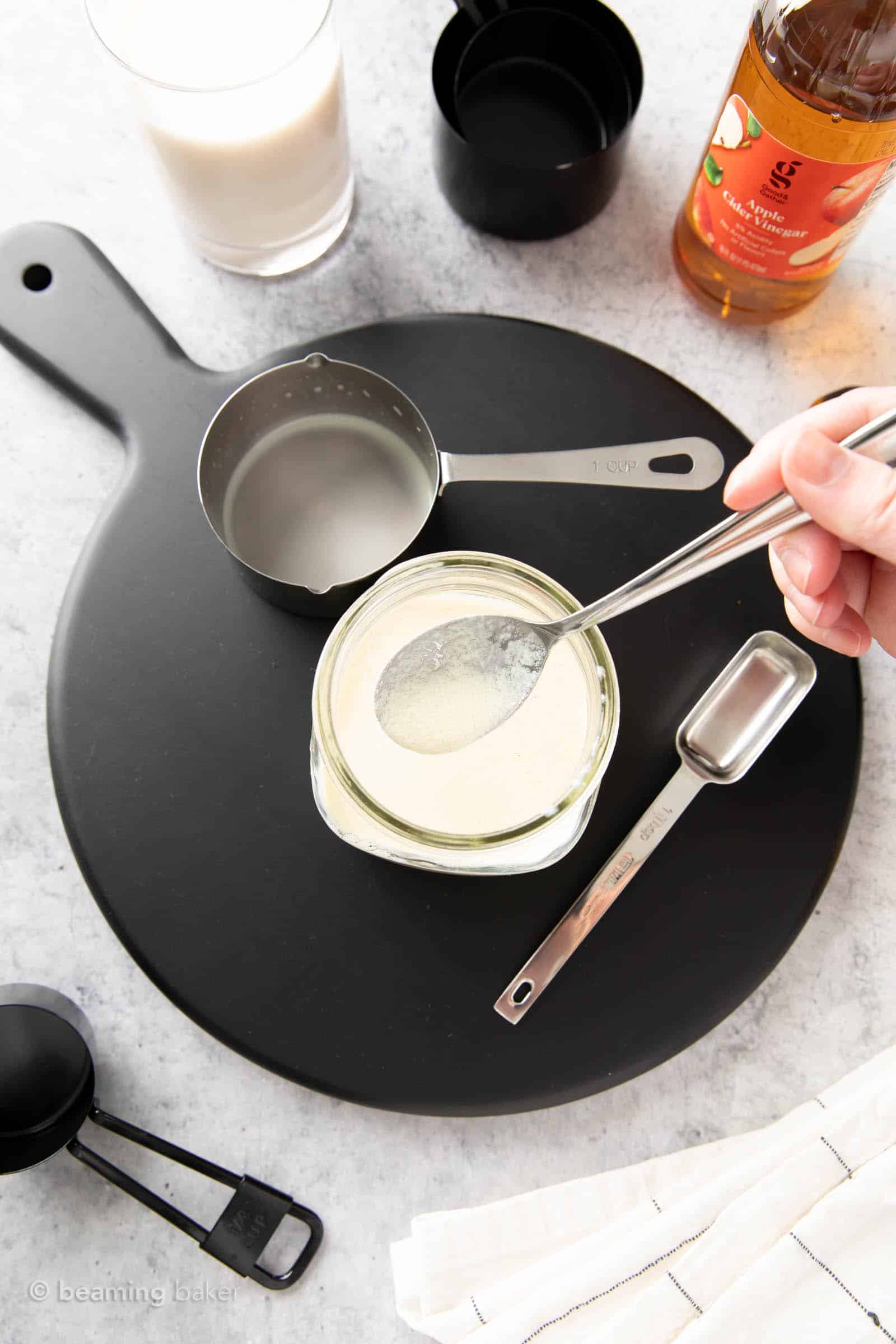 A hand holding a spoon of curdled vegan buttermilk with grainy bits of buttermilk visible on the spoon