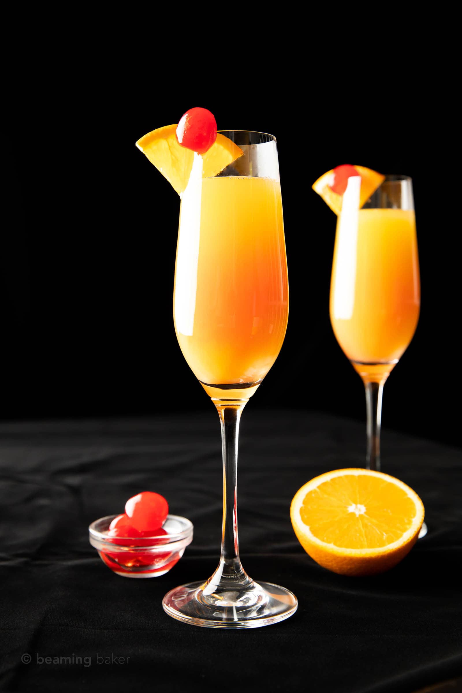 two sunrise mimosas in champagne flutes garnished with cherries