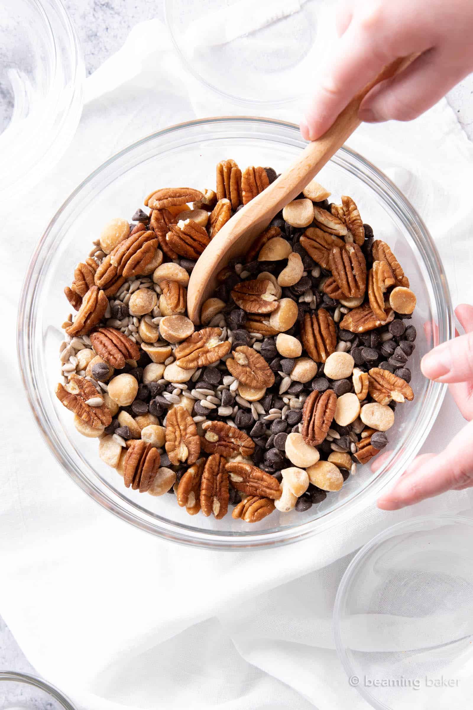 closeup of hands stirring together this keto trail mix recipe with a wooden spoon