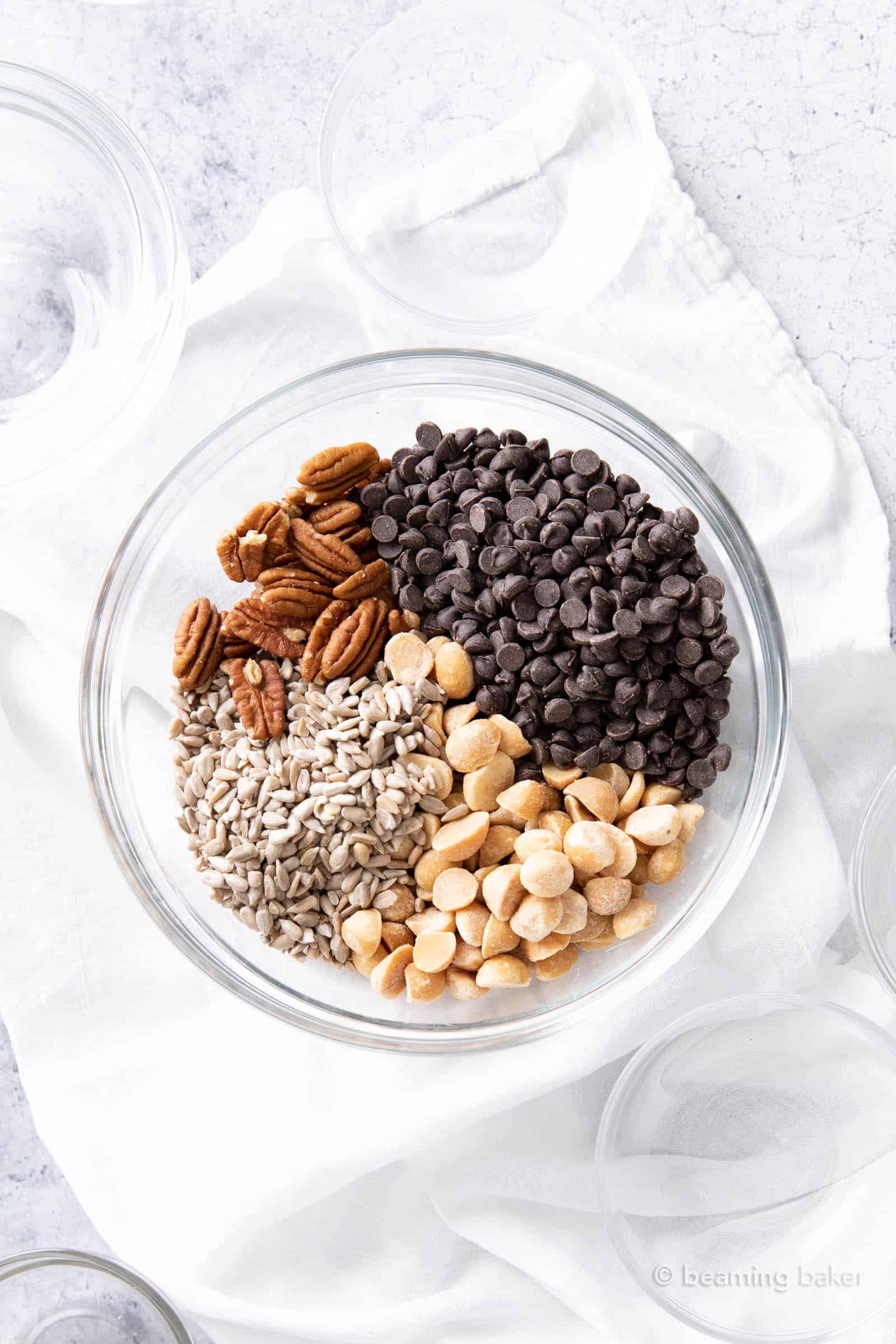 empty bowls surrounding a mixing bowl holding the ingredients for homemade keto trail mix