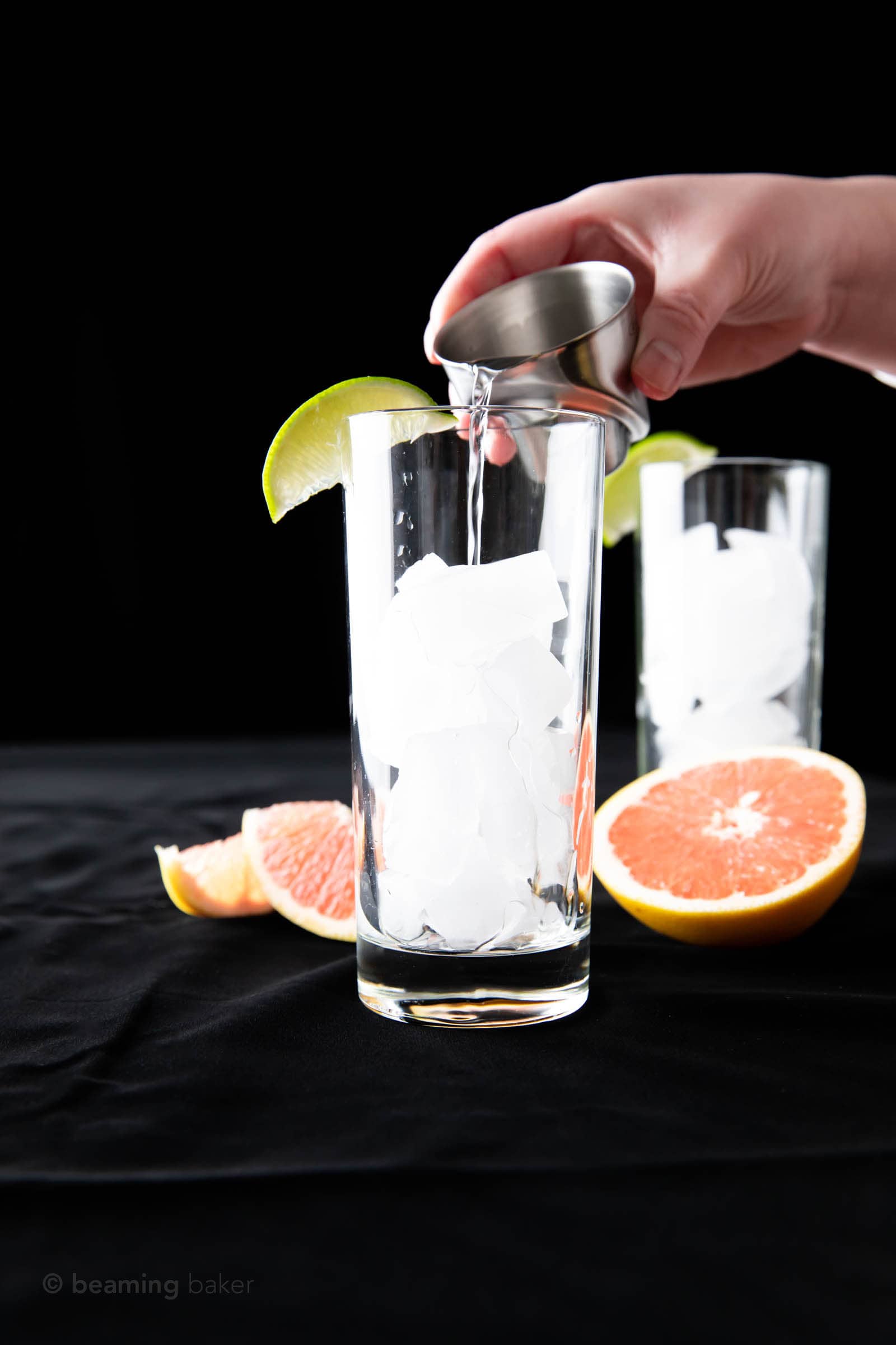 pouring gin from a measuring jigger into a highball glass for a greyhound cocktail recipe