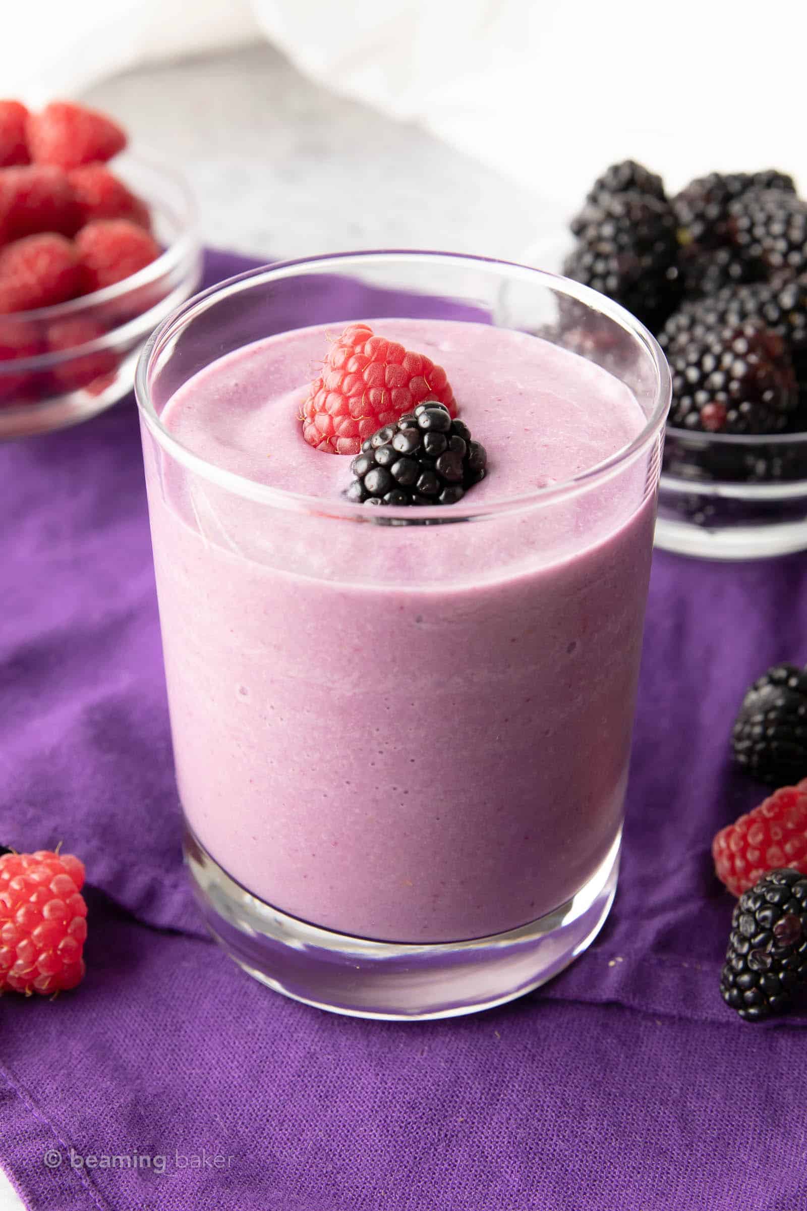 Glass of keto berry smoothie on a purble cloth with cups of fruit in the background