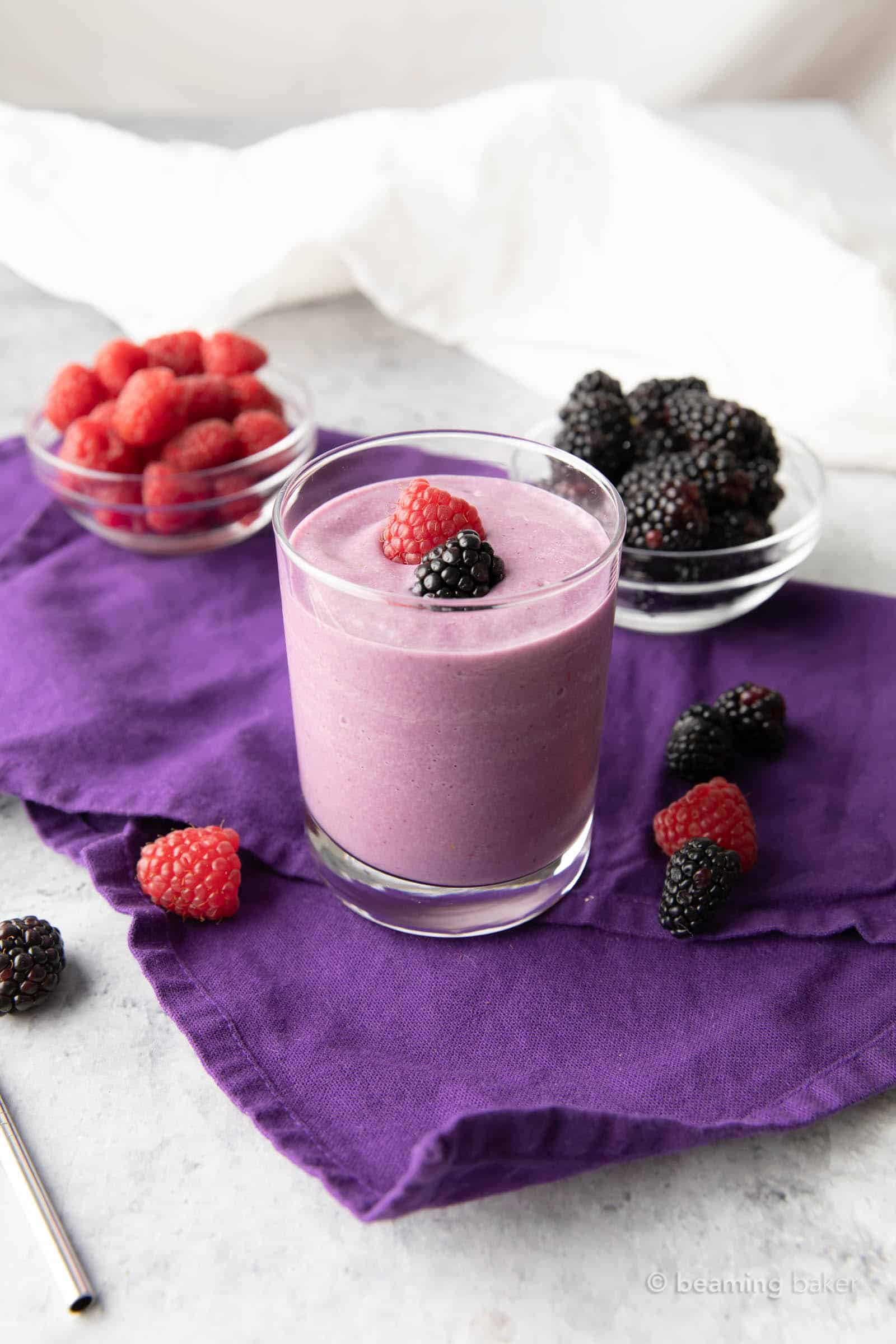 Low carb berry smoothie on a purpble tablecloth with raspberries and blackberries surrounding it