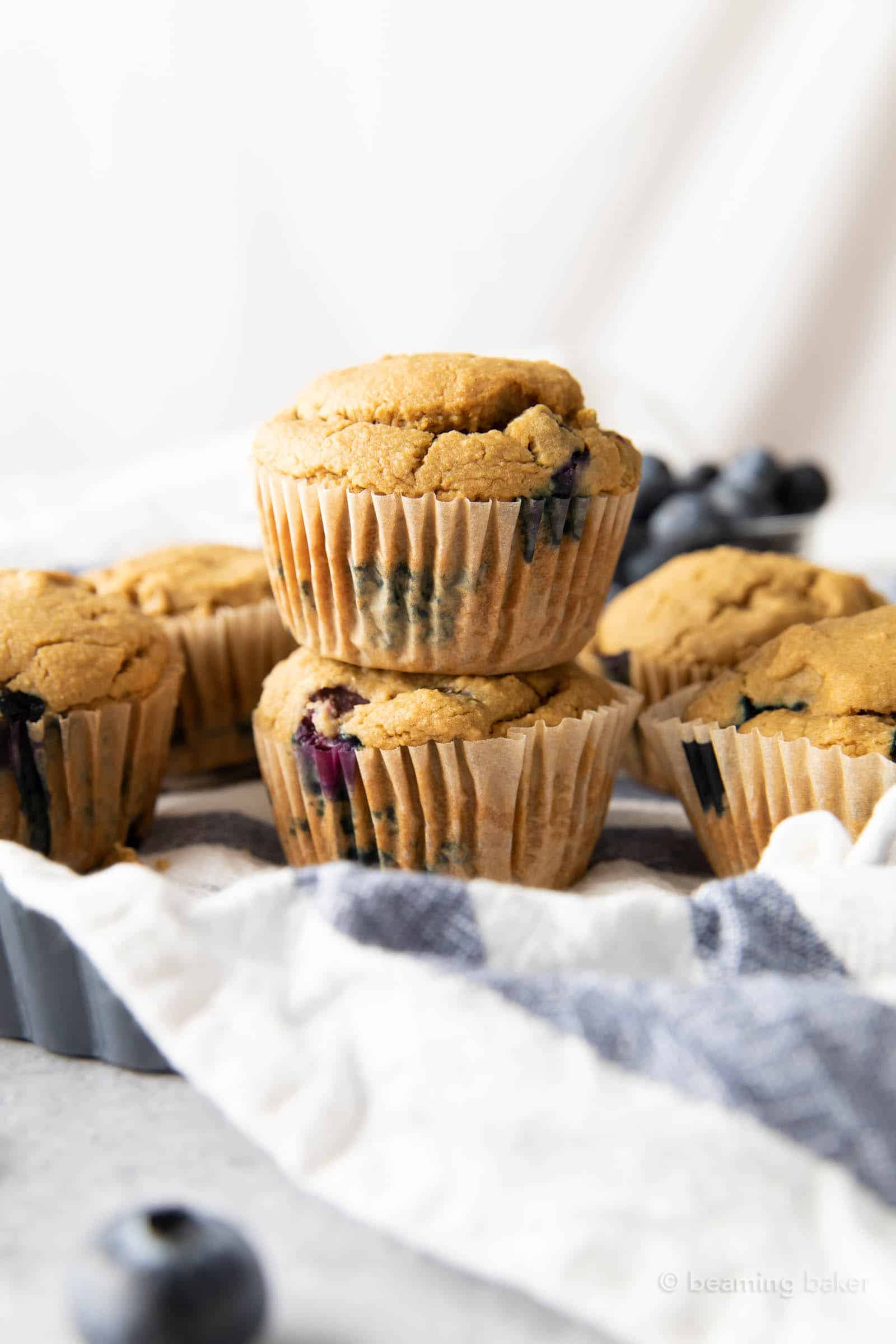 Two oatmeal flour blueberry muffins stacked on each other with more muffins around them