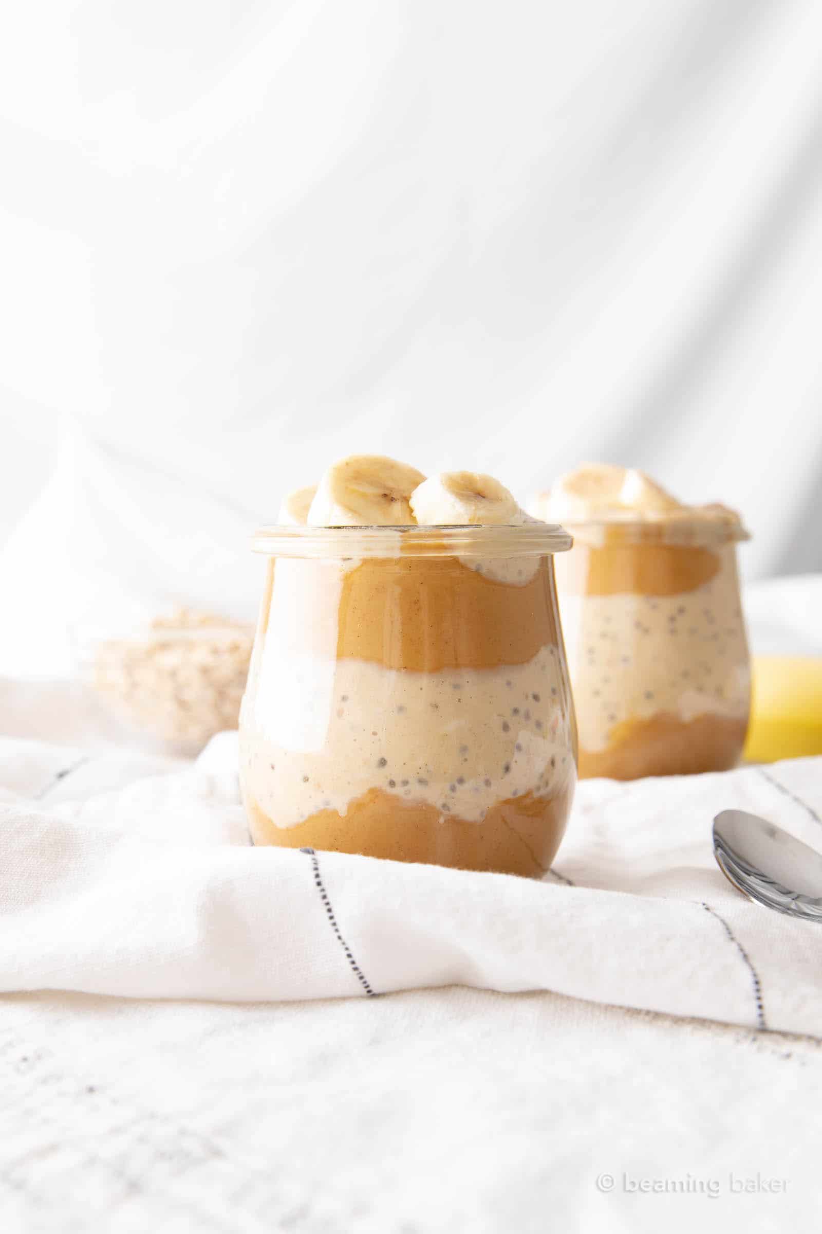 Two jars of peanut butter banana overnight oats on a table with cloth napkins nearby