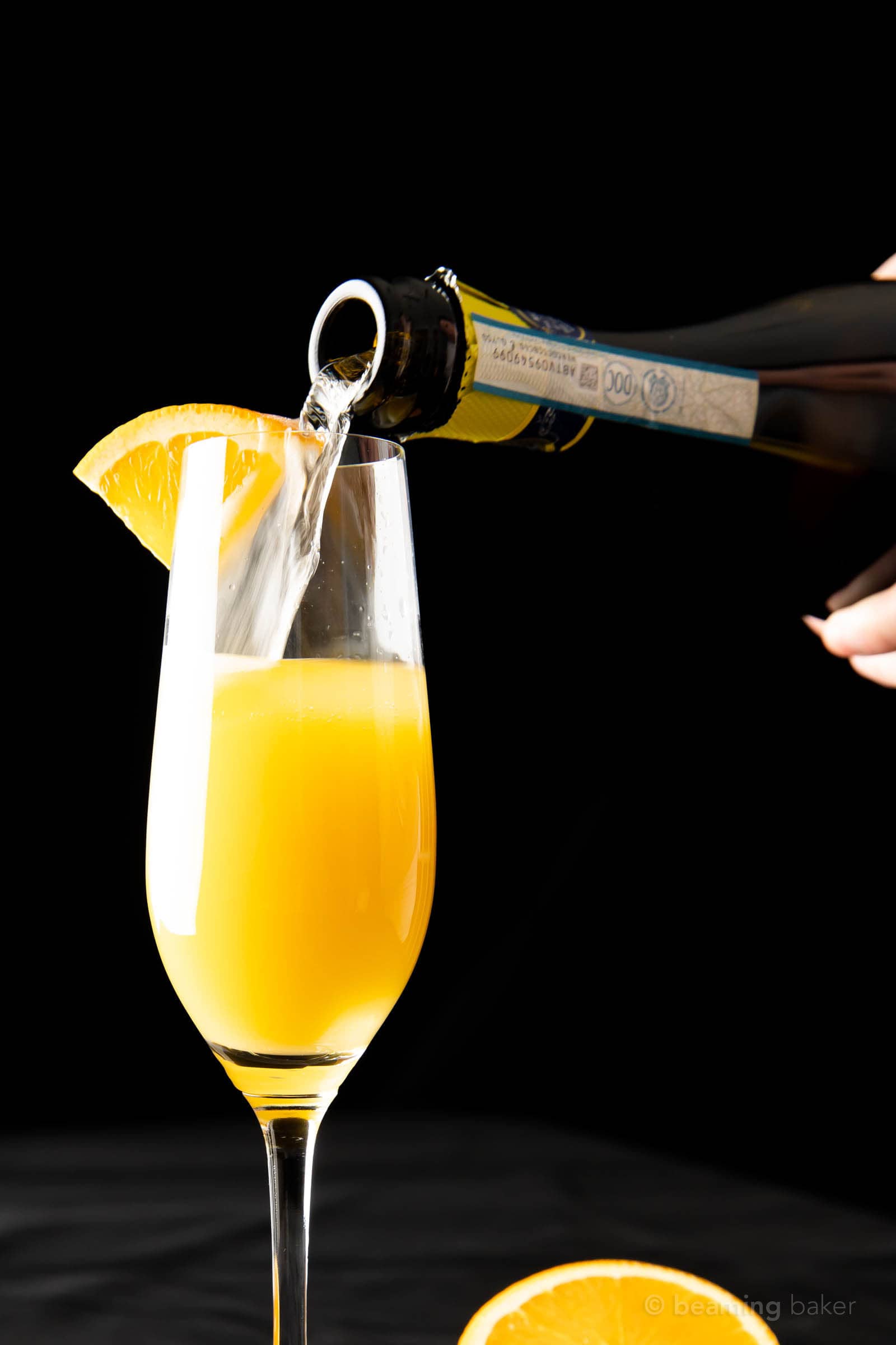 closeup shot of hand pouring prosecco into a flute filled halfway with orange juice for a mimosa