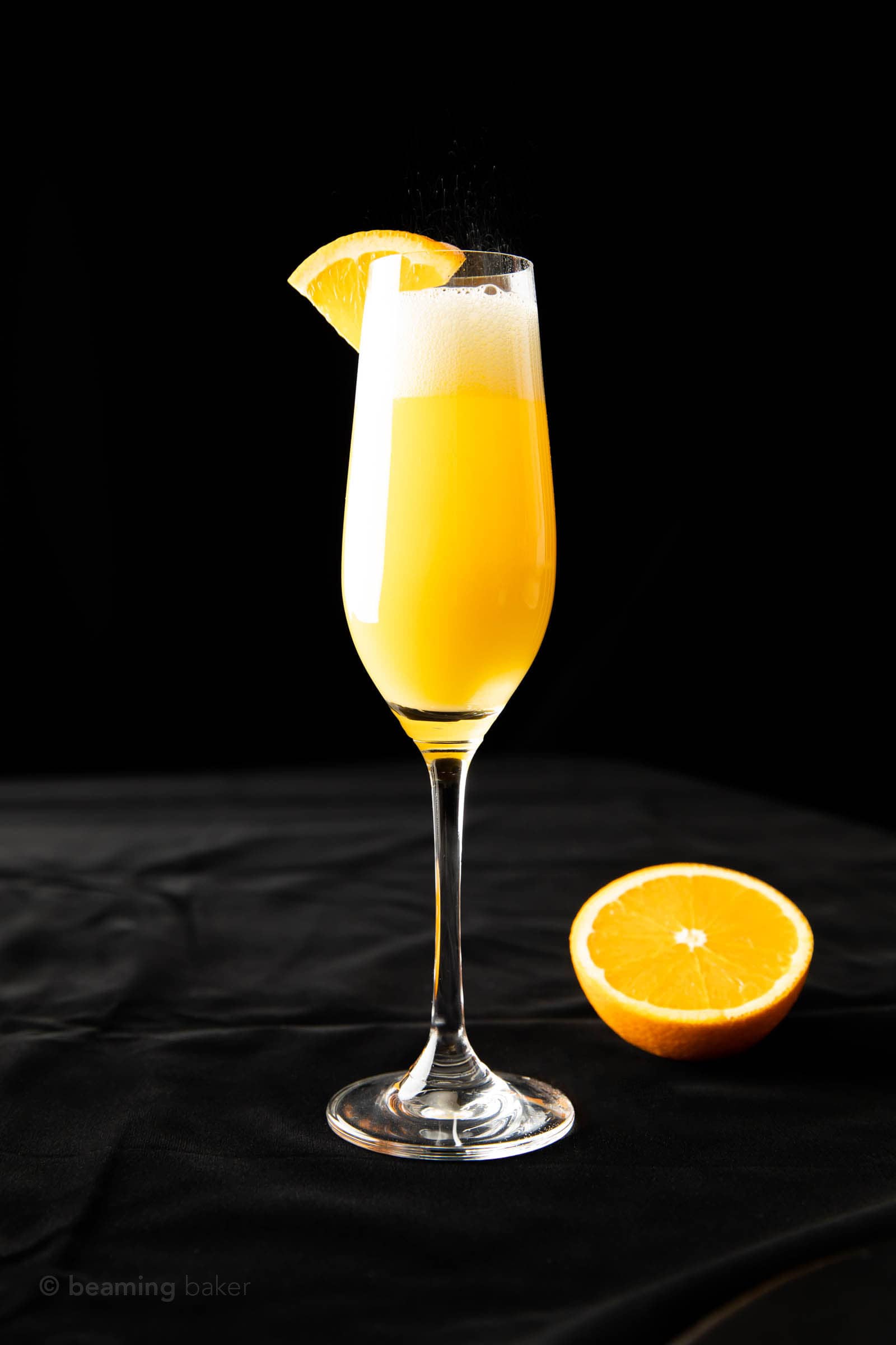 full shot of mimosa drink in a champagne flute with half an orange