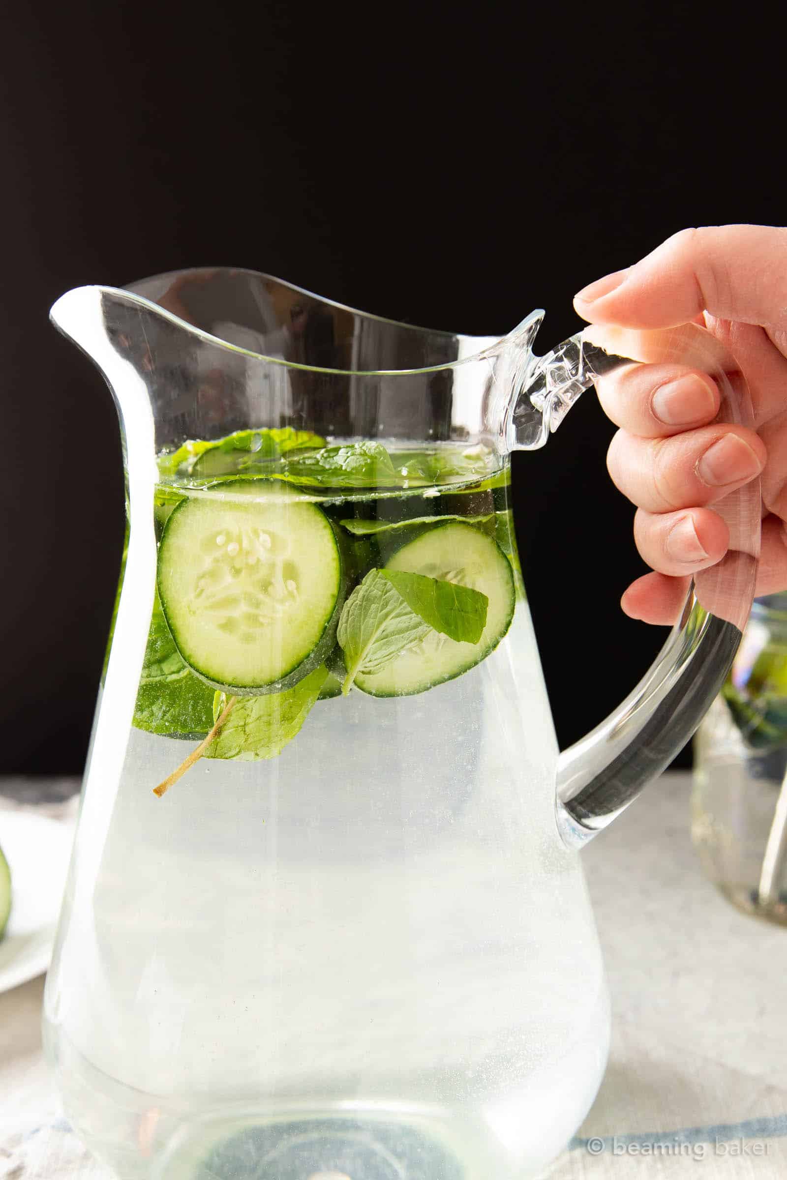 Hand holding a pitcher of cucumber and mint water