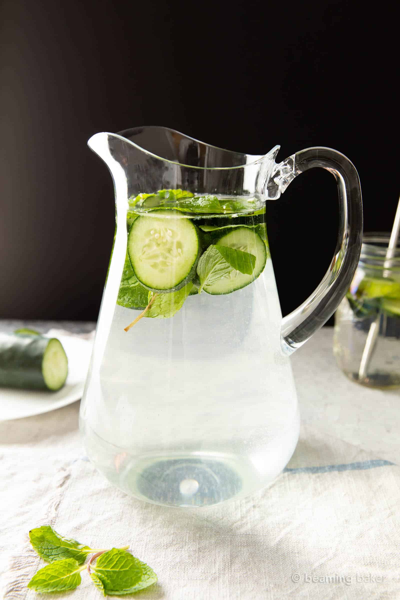 Pitcher of cucum er mint water with half a cucumber and some mint leaves sitting nearby on the table