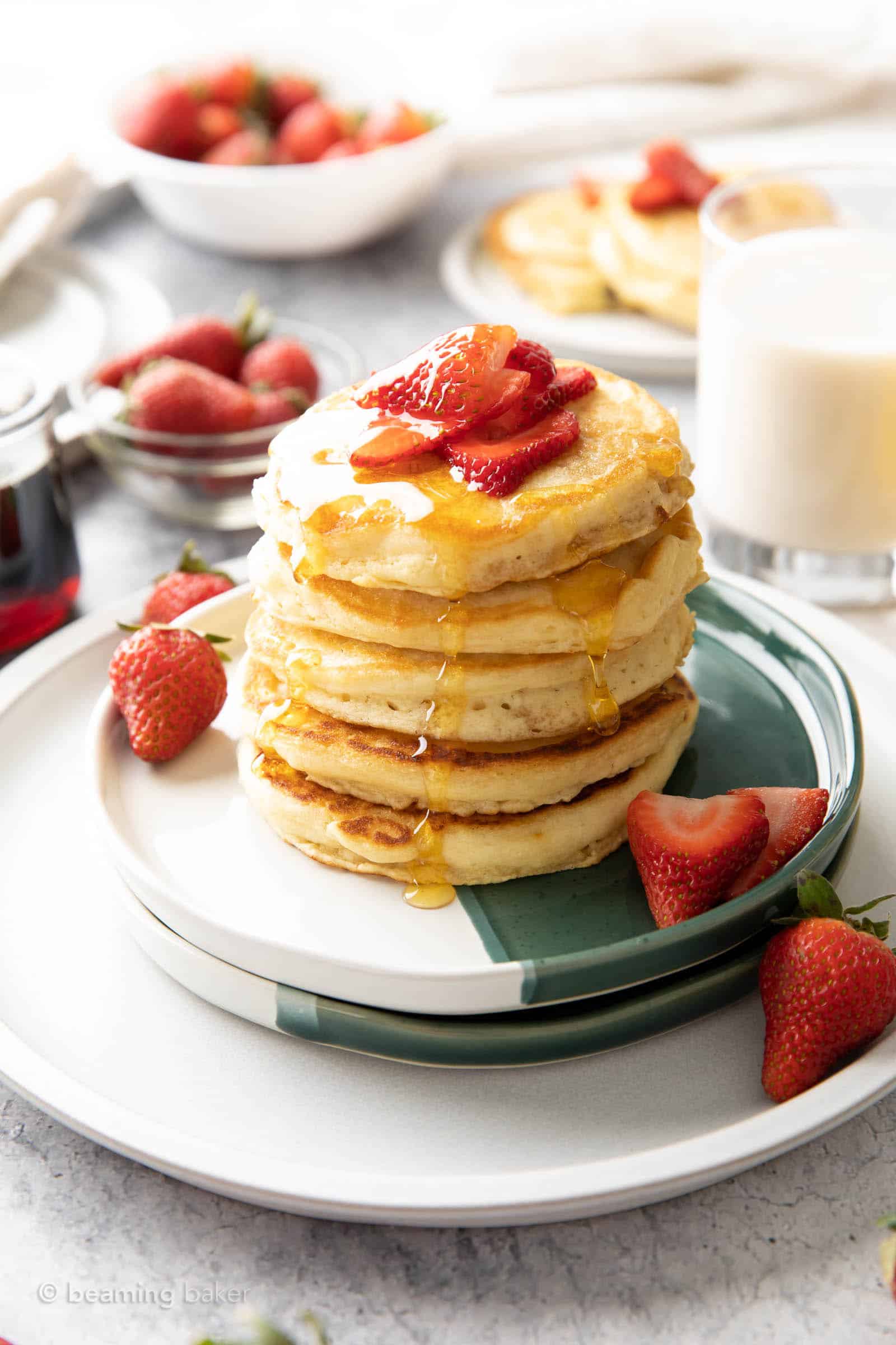 fluffy strawberry pancakes served in a stack with a pitcher of maple syrup and fresh strawberries