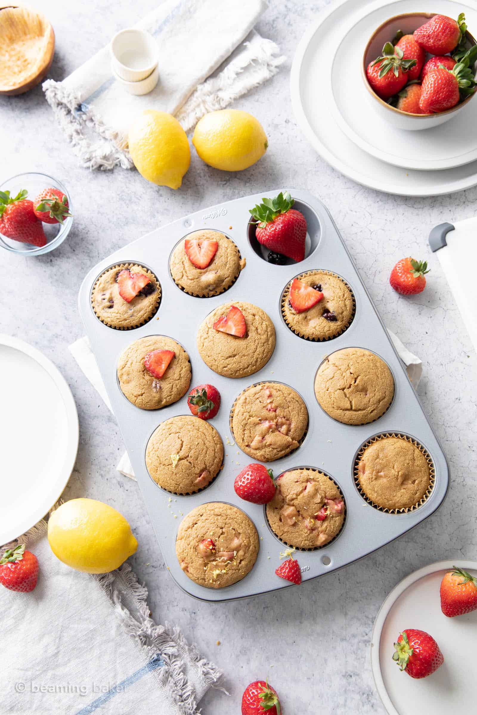 overhead shot of fresh-baked strawberry lemon muffins with lemons and strawberries in bowls