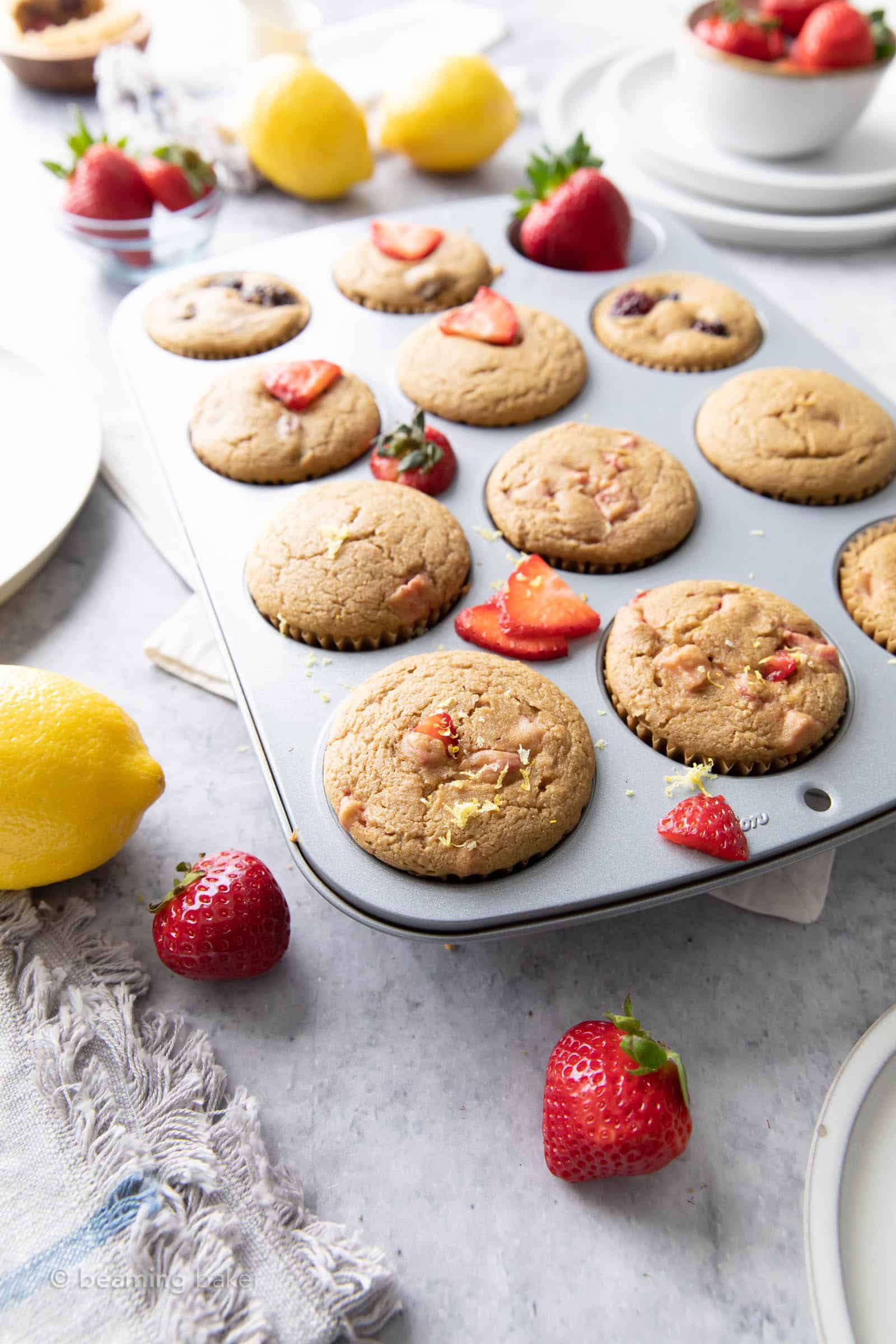 far angled shot of strawberry lemon muffins cooling in muffin pan with serving plates