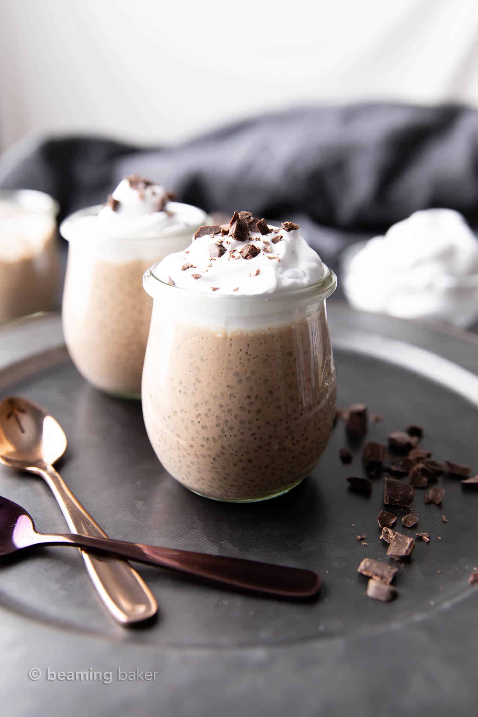 two jars of chocolate chia seed pudding on a dark gray serving plate and two spoons