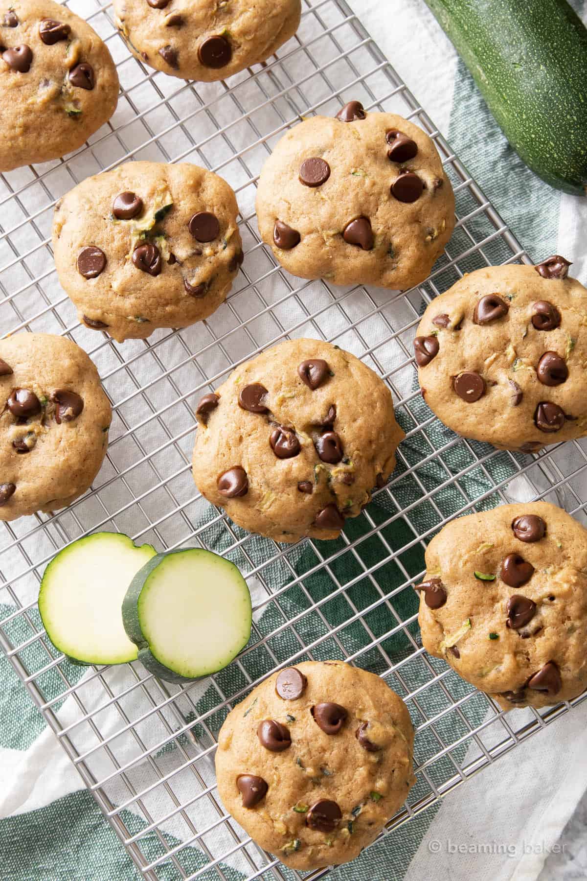 Half a dozen zucchini chocolate chip cookies with fresh zucchini on a white and green towel