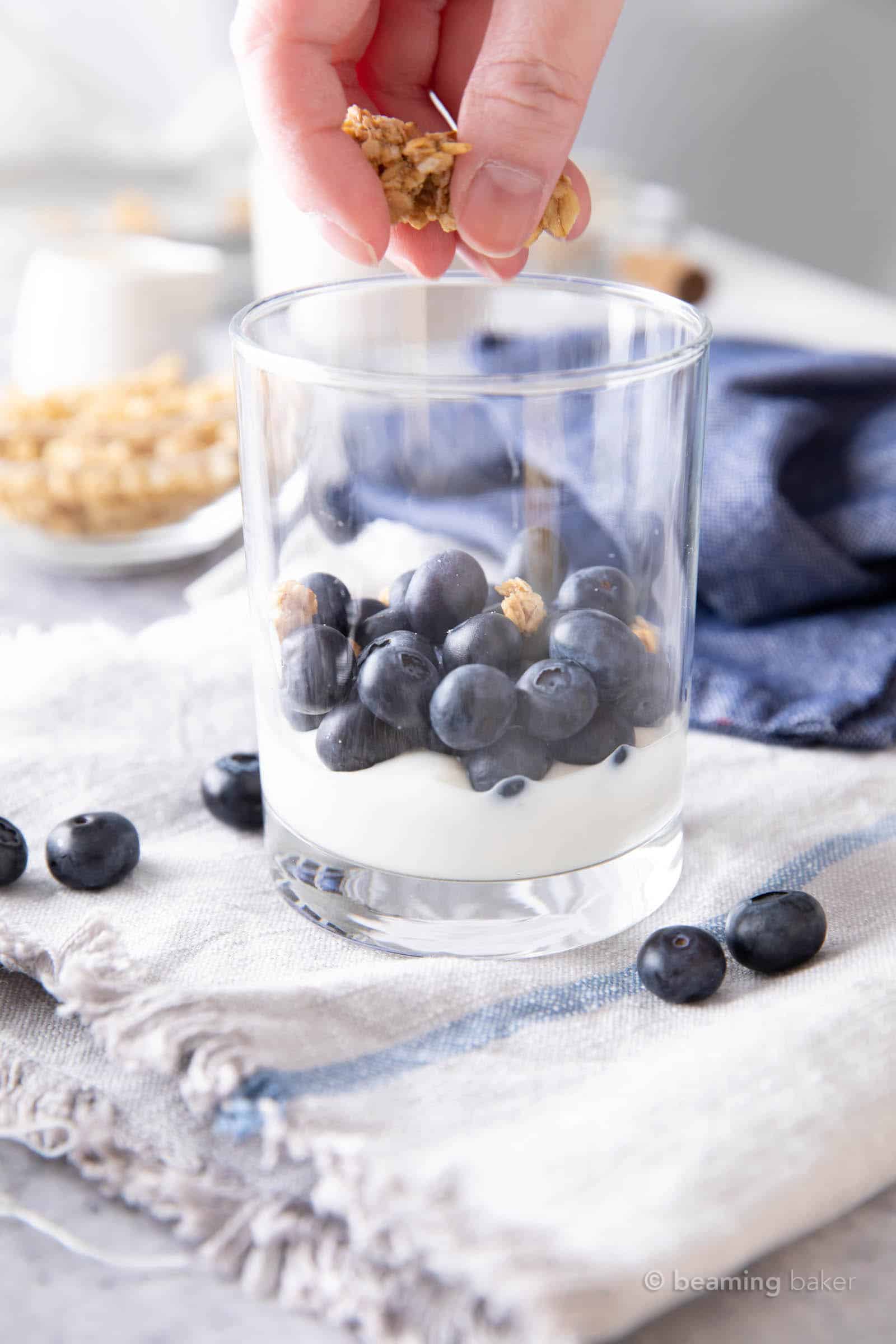 Hand sprinkling granola over blueberry layer in blueberry yogurt parfait