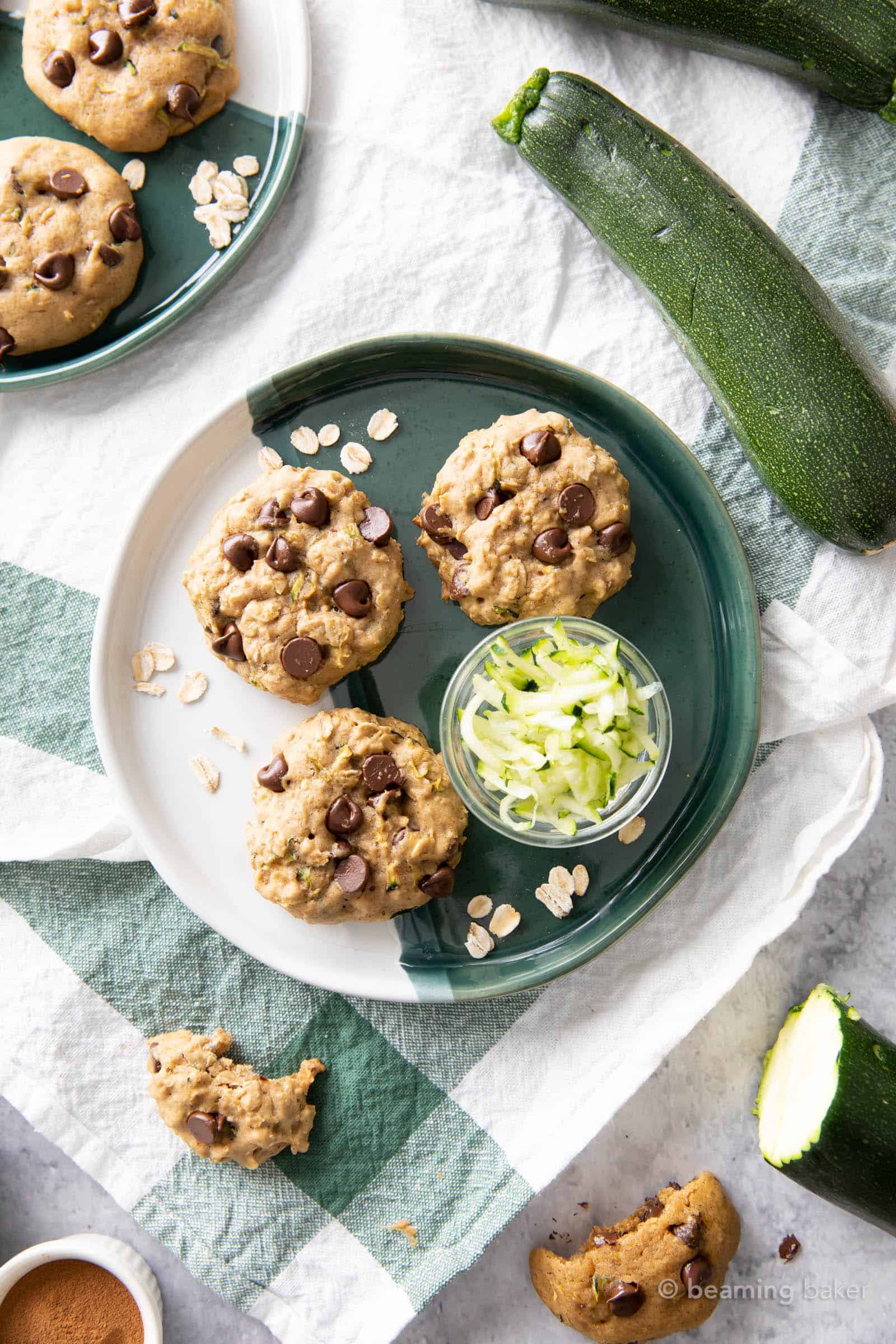 kitchen table filled with chocolate chip zucchini oatmeal cookies, fresh zucchinis and green napkins