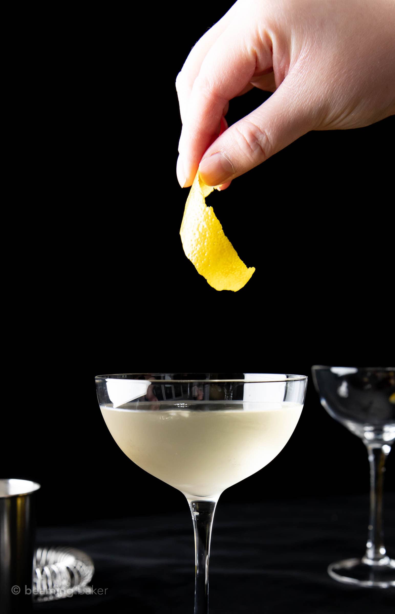 Hand dropping lemon garnish into cocktail glass