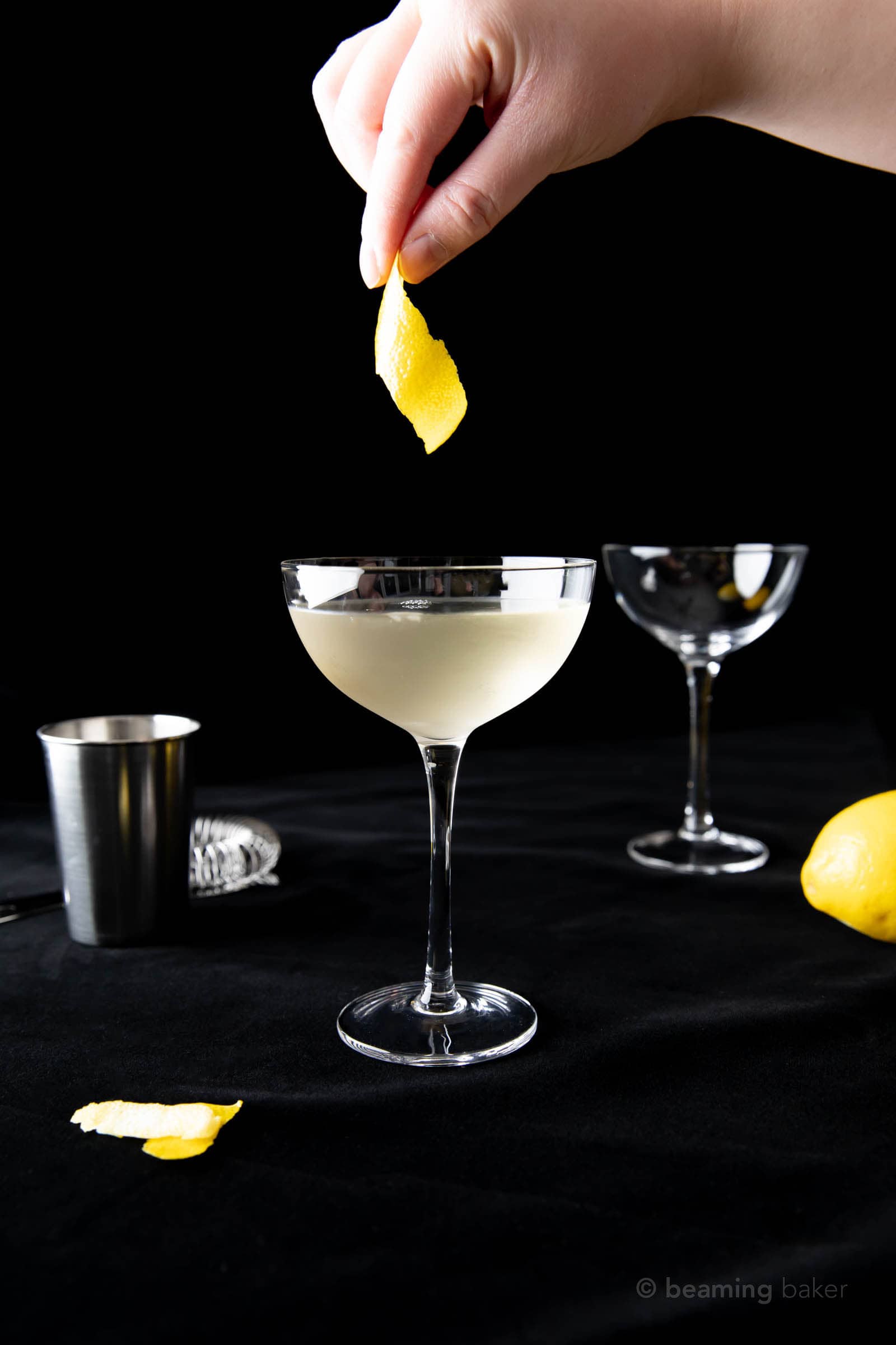 Hand dropping a lemon peel into the rim of a coupe glass to finish off the martini