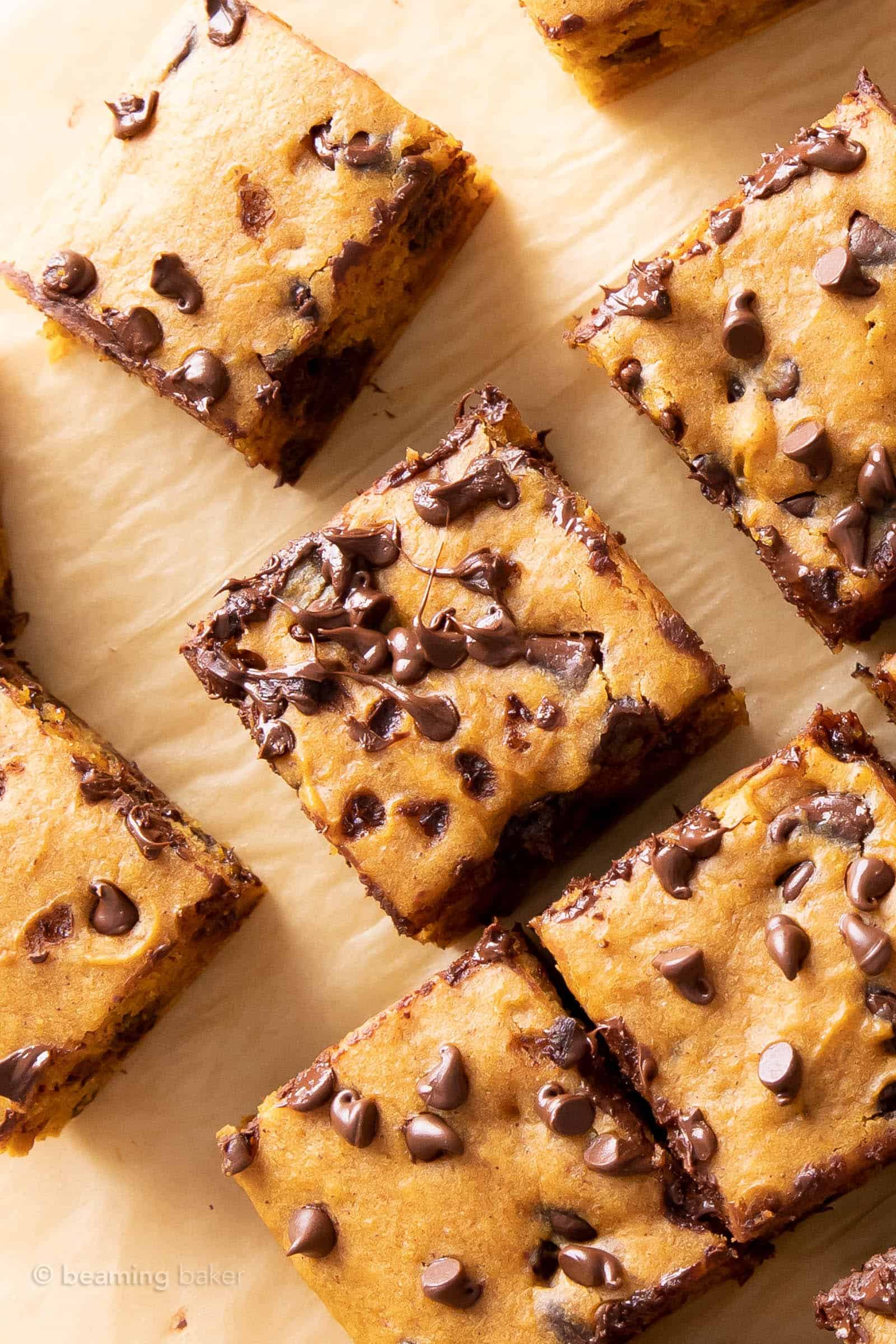 Melty chocolate chips adorn fresh-baked pumpkin bars on brown parchment paper