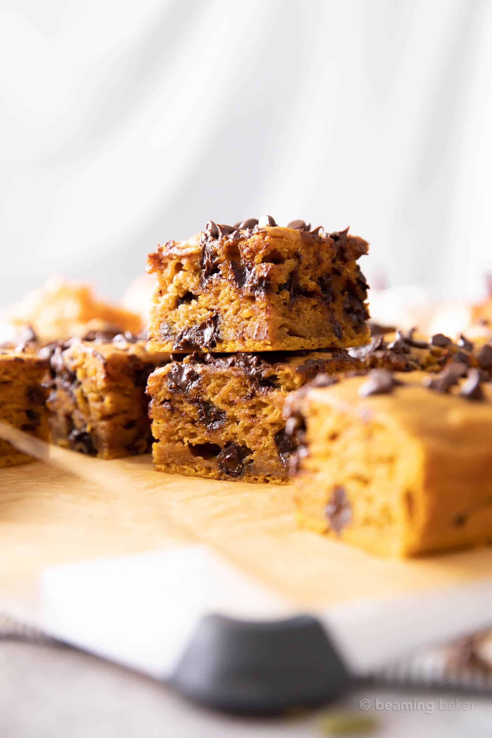 two pumpkin chocolate chip bars on a cutting board with more bars against a white backdrop