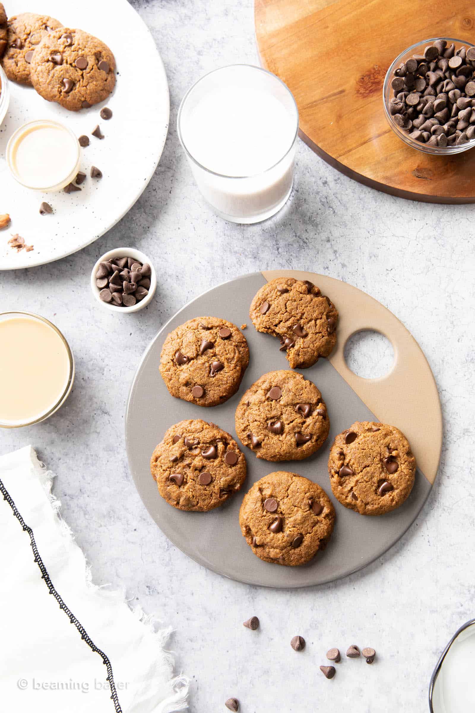 Circular serving board with tahini cookies, a glass of milk, a bowl of chocolate chips, and tahini