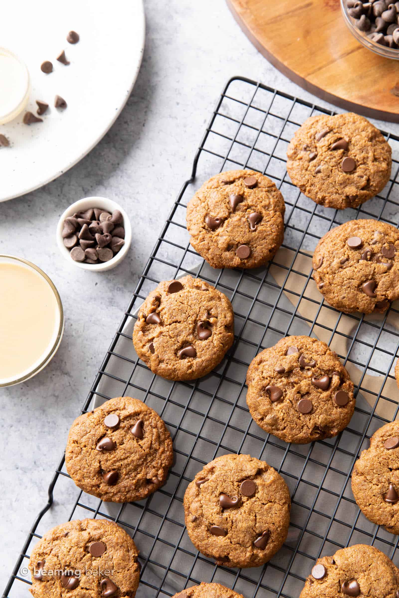 Vegan tahini chocolate chip cookies on a black cooling rack with a bowl of tahini and cutting board