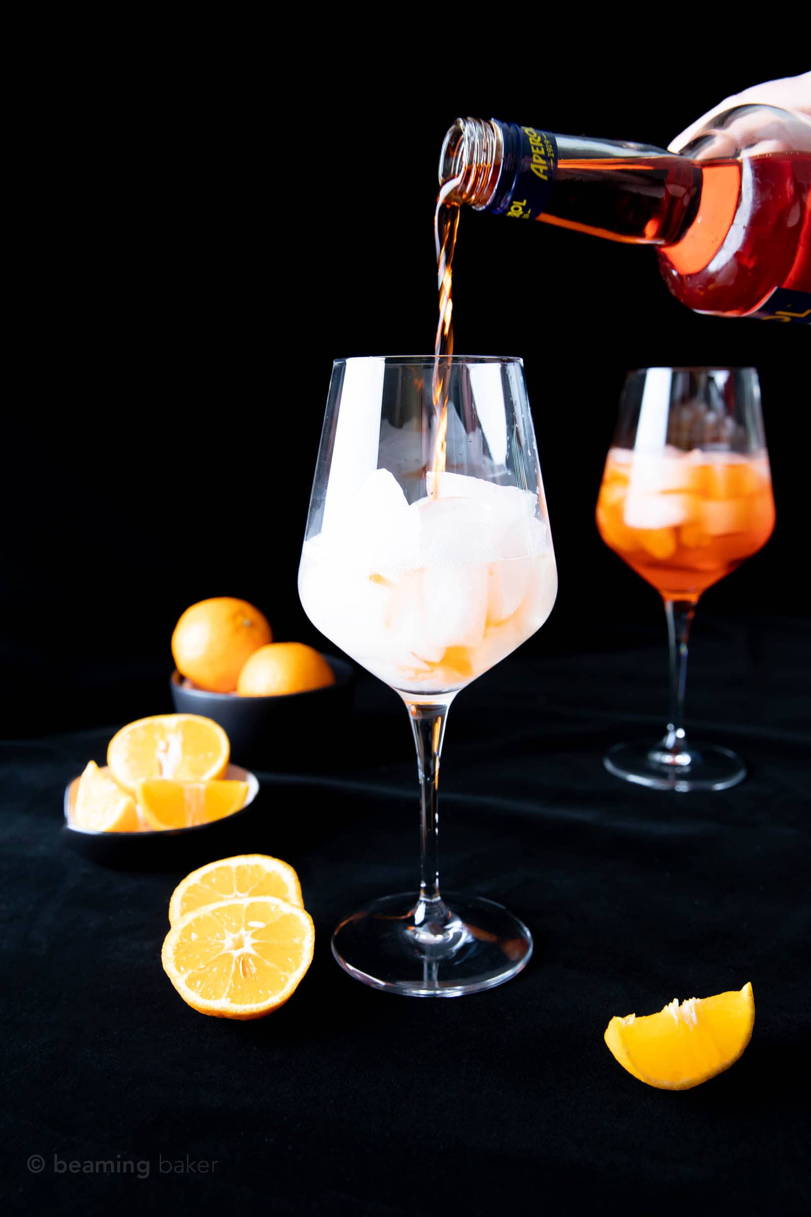 hand pouring Aperol into glass filled with ice and Prosecco