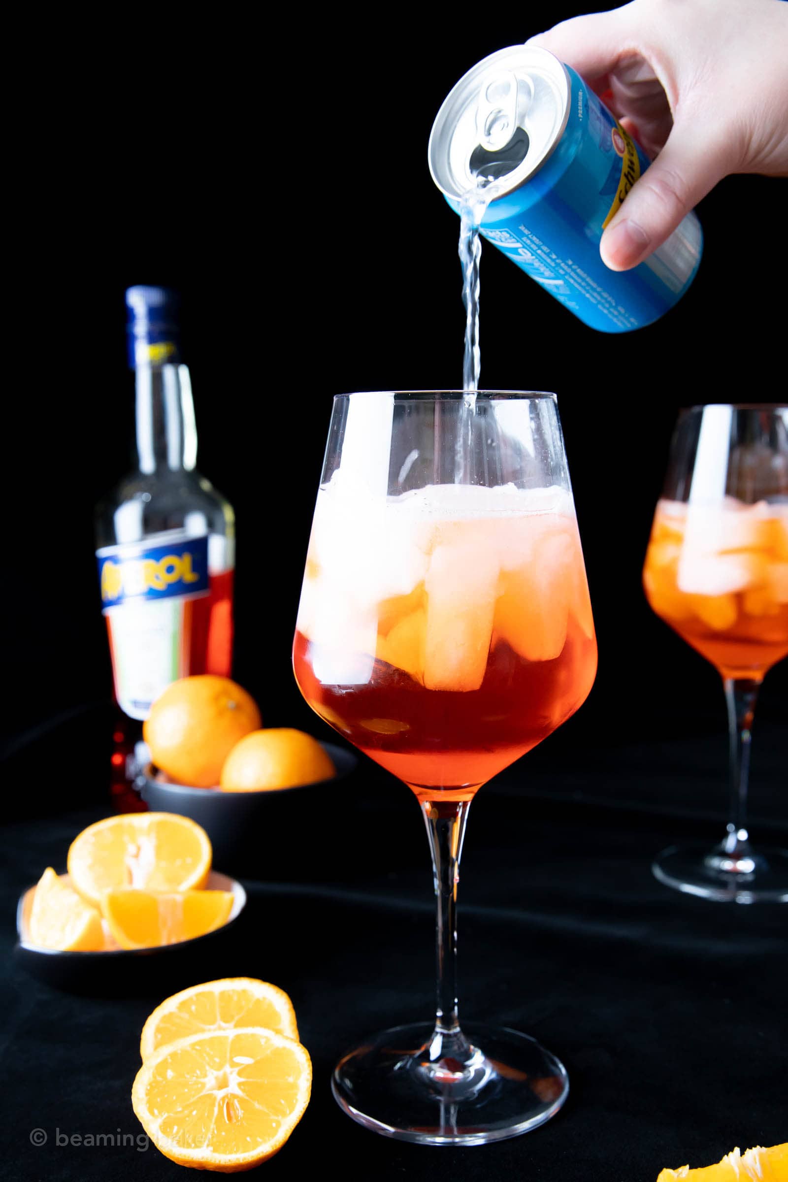 hand pouring a can of club soda over the Aperol into the wine glass