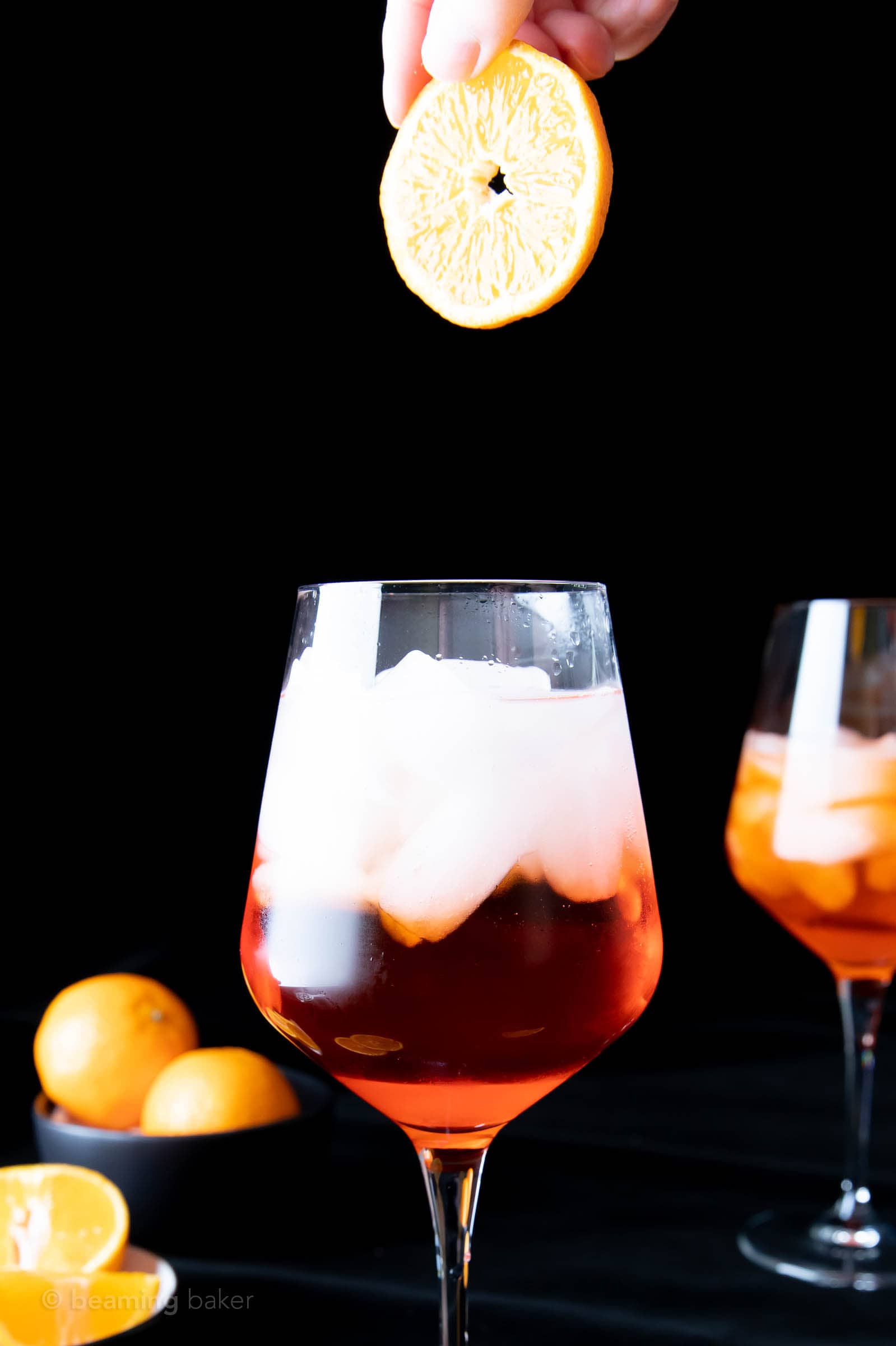 fingers dropping orange slice garnish into Aperol Spritz