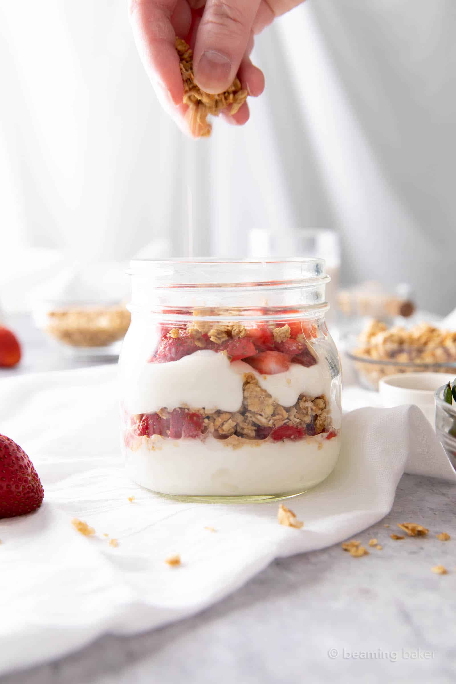 Hand sprinkling granola over strawberries to create another parfait layer