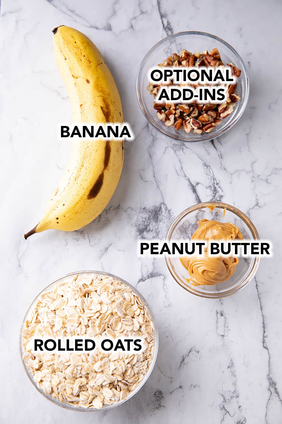 ingredients for peanut butter banana cookies in bowls including a banana, peanut butter, rolled oats, and a bowl of nuts