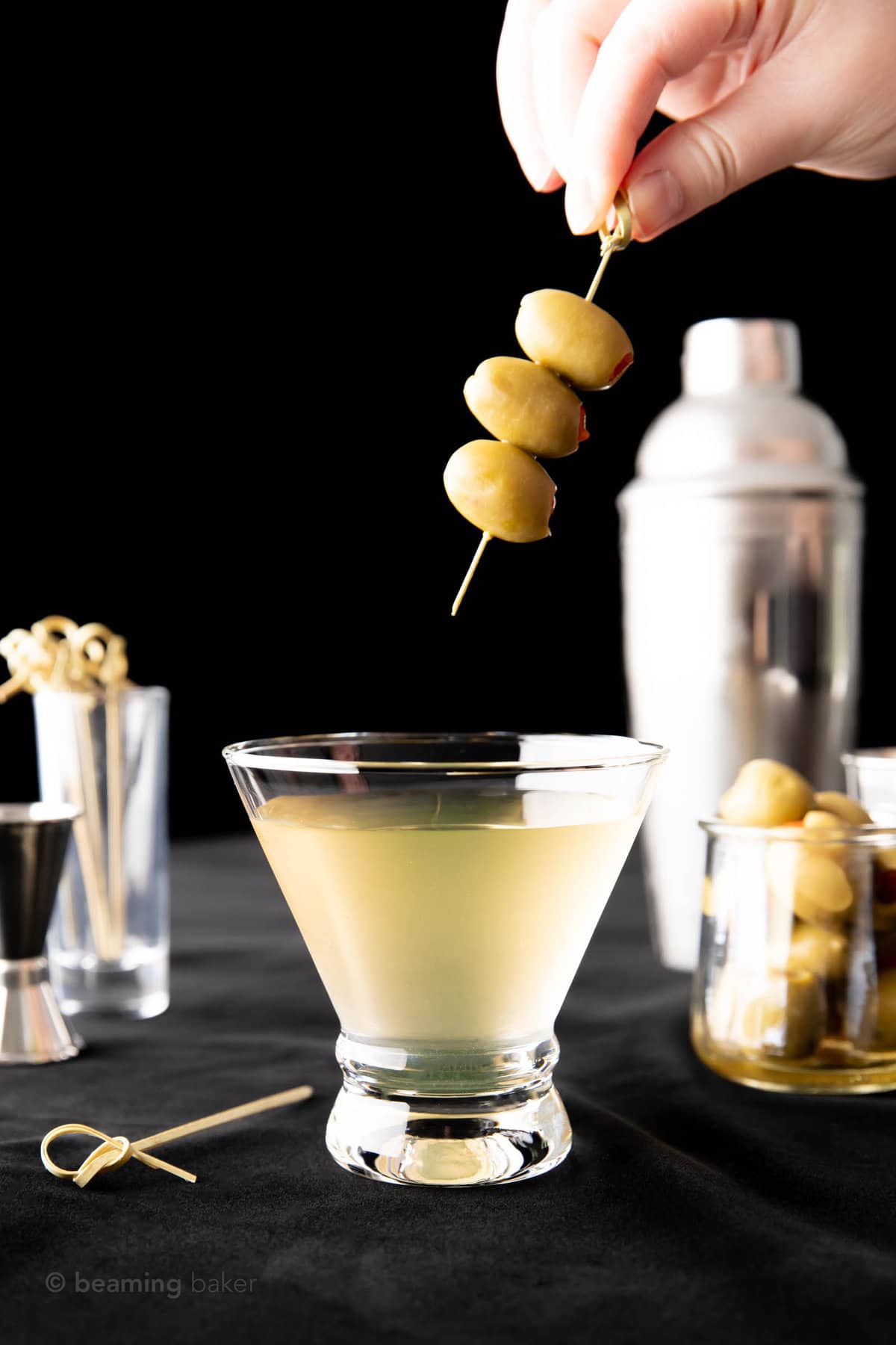 hand dropping an olive skewer into a short cocktail glass