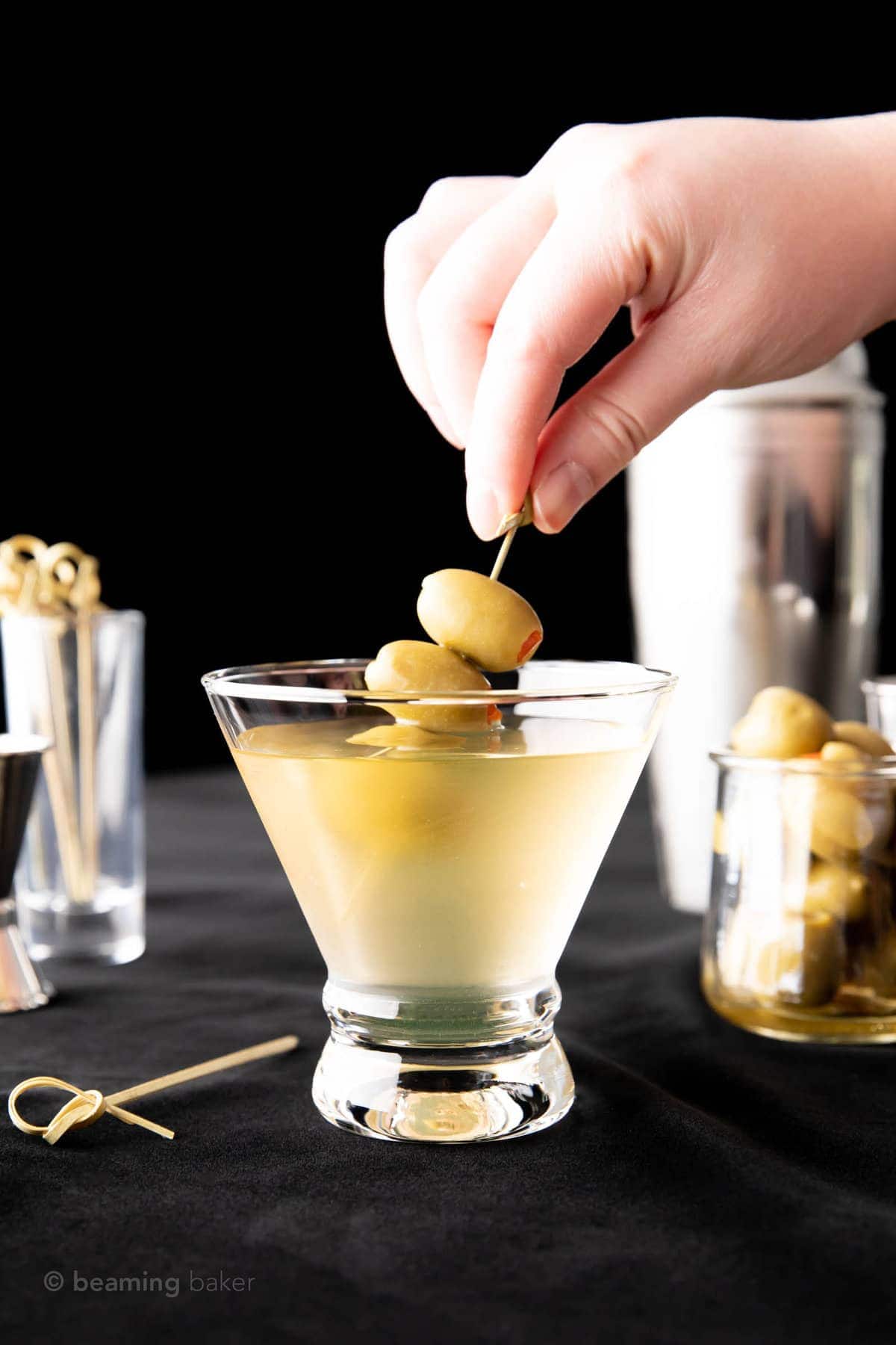 hand holding olive skewer that's nearly submerged in the cocktail