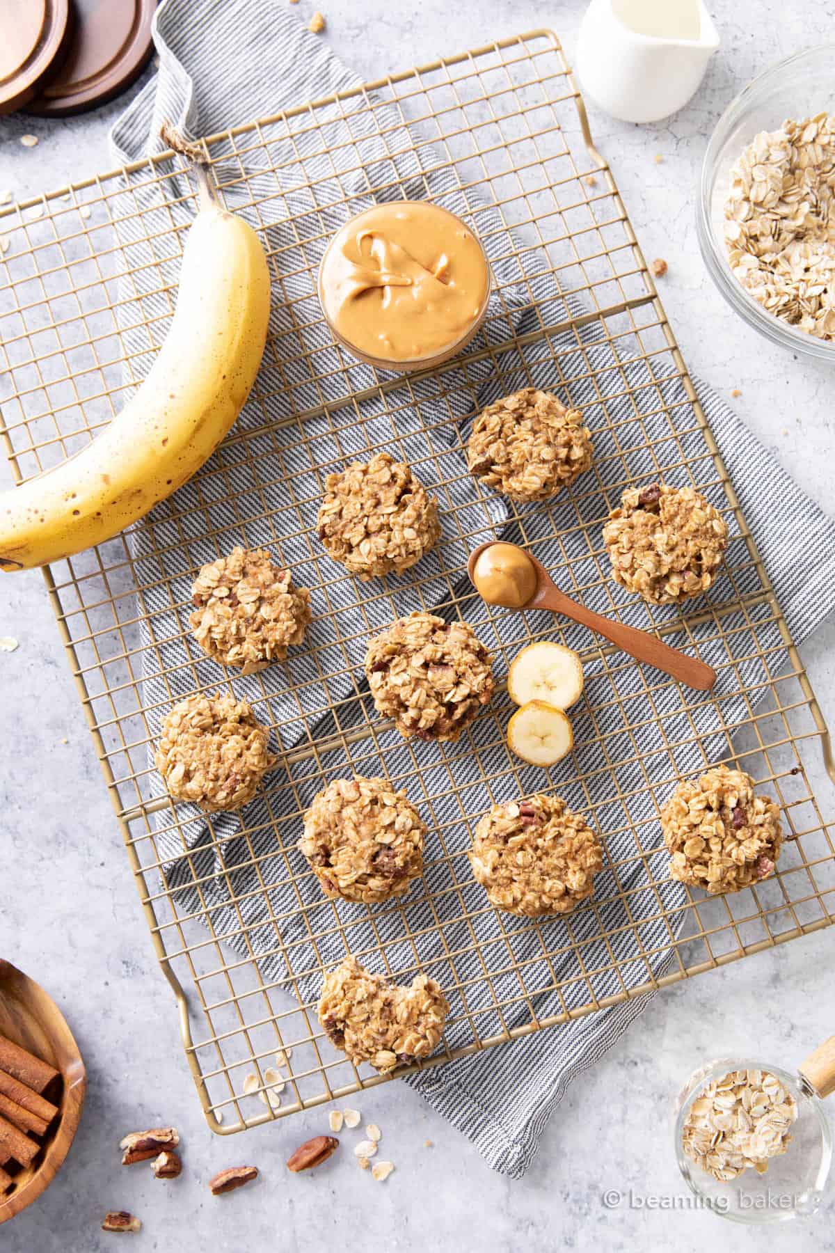 A gold cooling rack with cookies, a banana, and a bowl of peanut butter