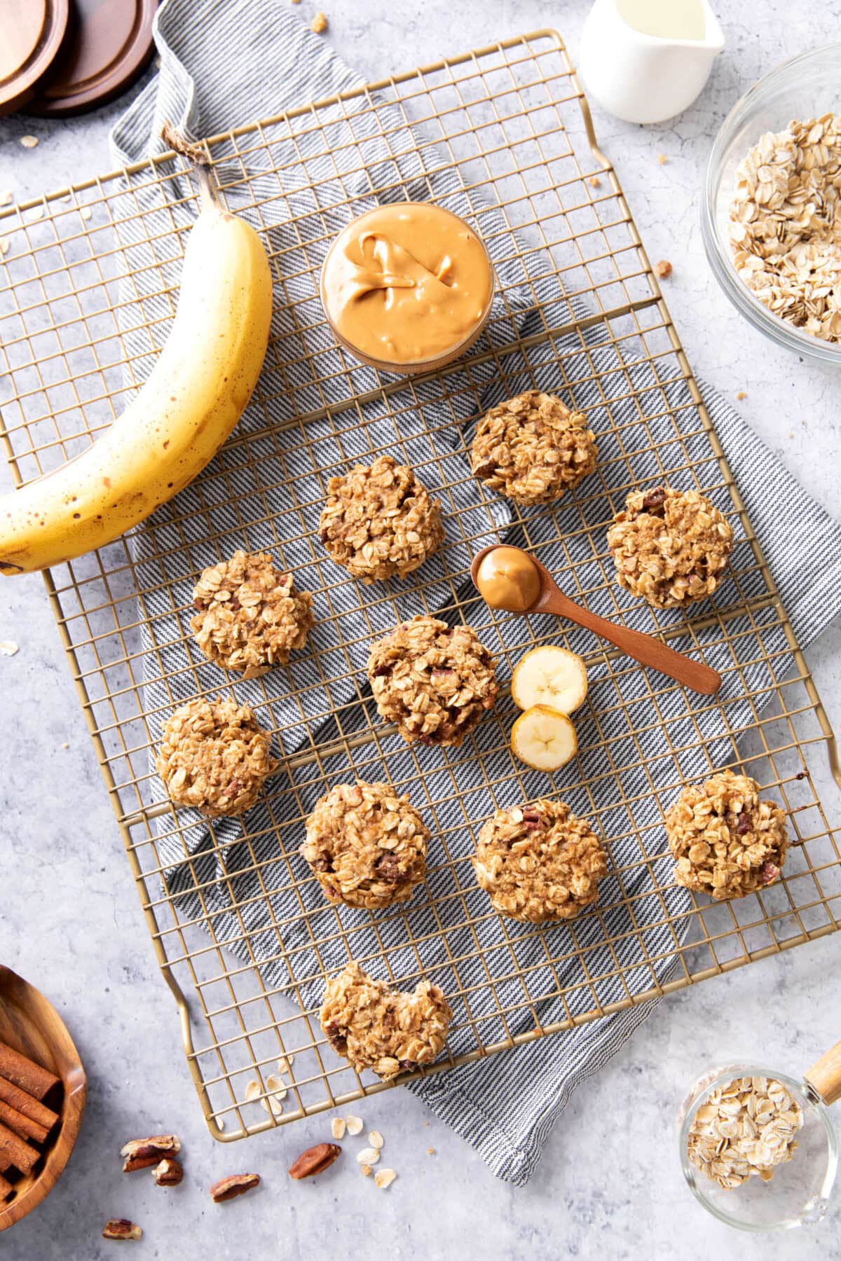 A gold cooling rack with cookies, a banana, and a bowl of peanut butter