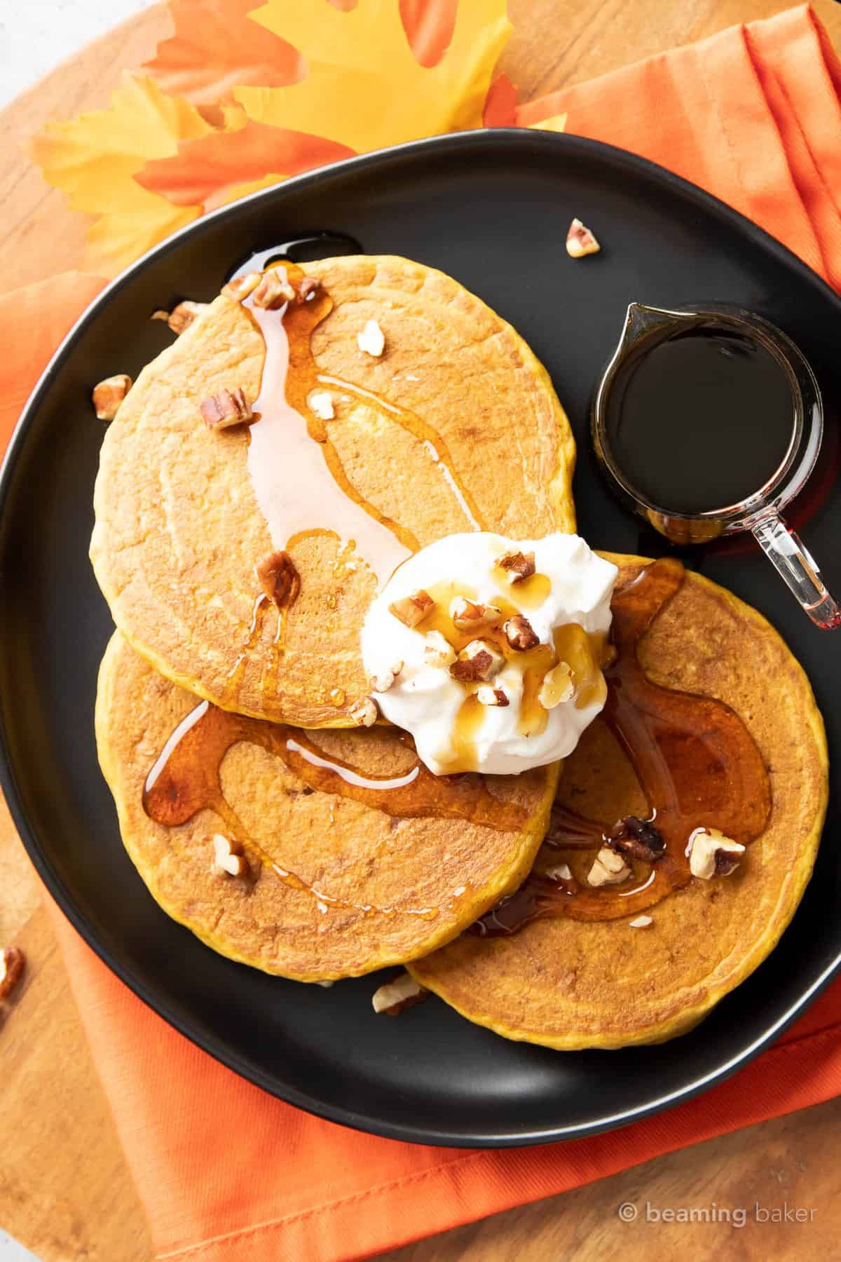 closeup of three pumpkin spice pancakes covered in maple syrup, whipped topping, and pancake syrup