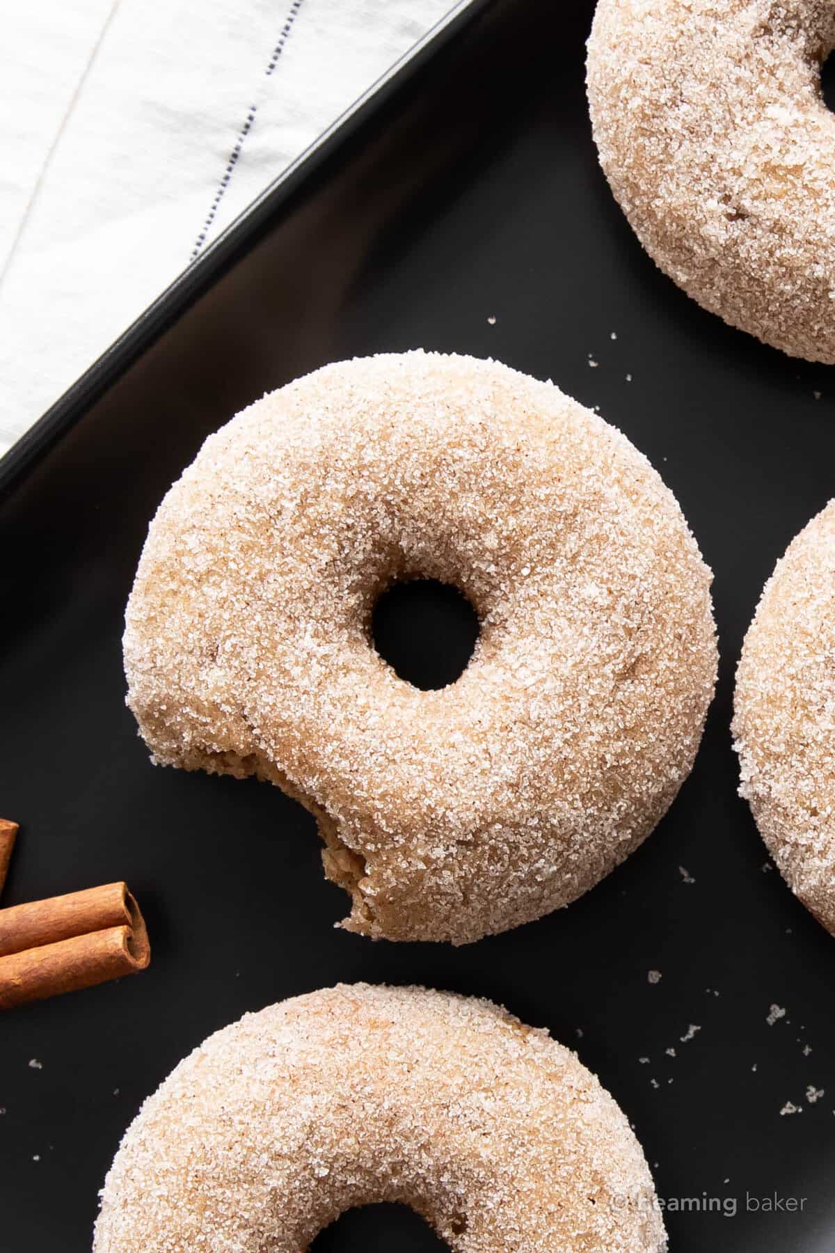 closeup of a bitten cinnamon sugar donut on a black serving tray