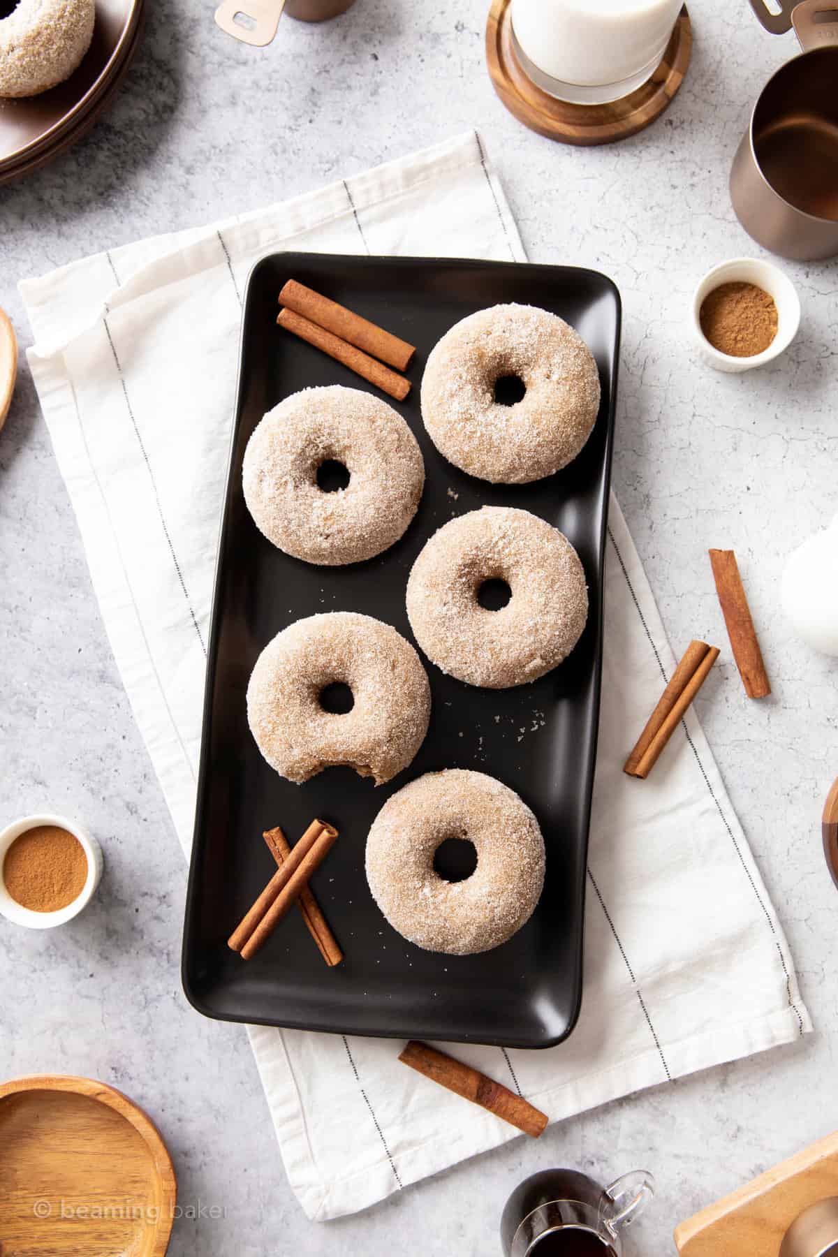 cinnamon sugar donuts on kitchen table with cinnamon sticks and bowls of sugar