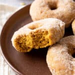 a bitten pumpkin donut on a brown plate