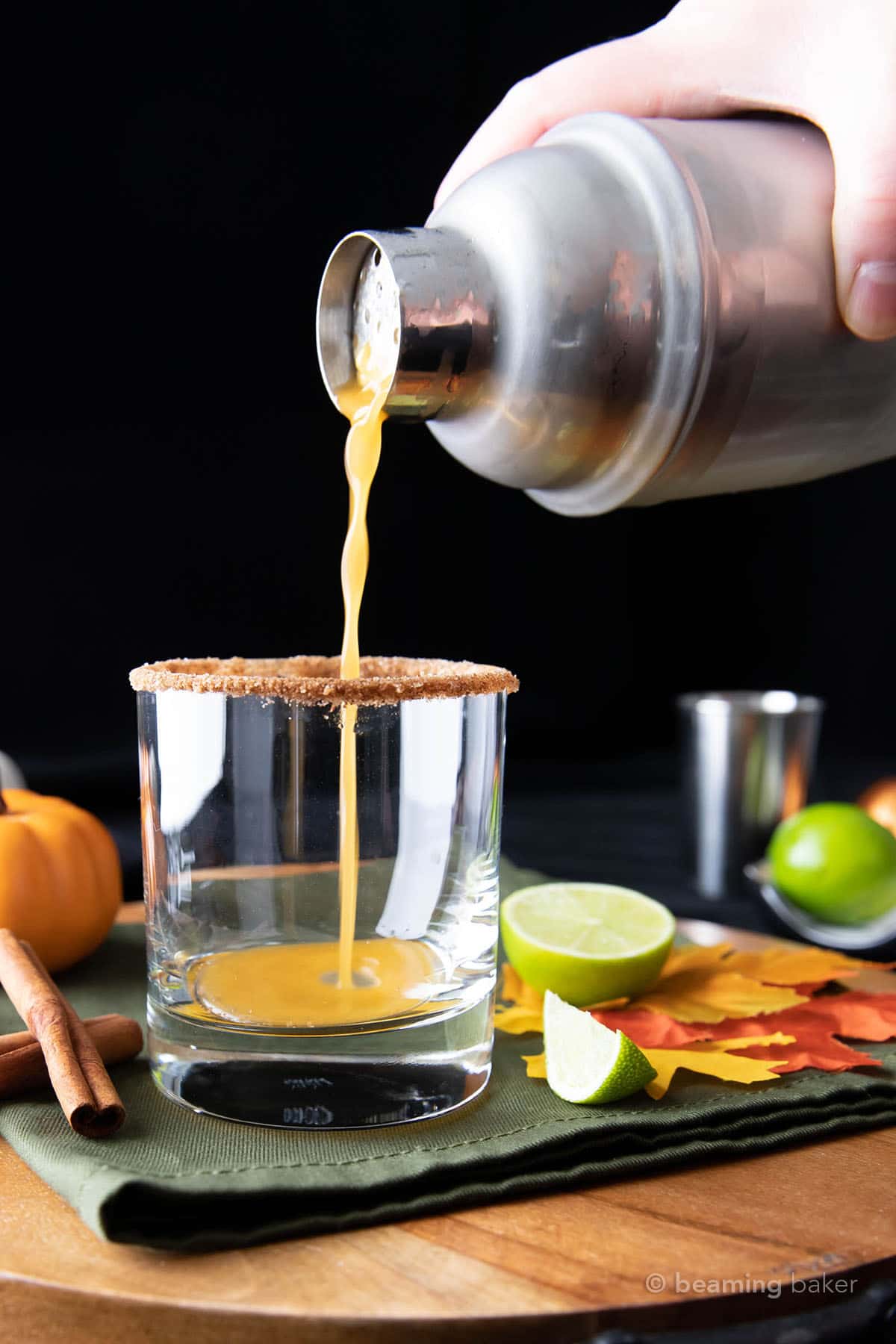 a hand pouring pumpkin spice margarita from a cocktail mixer into a glass