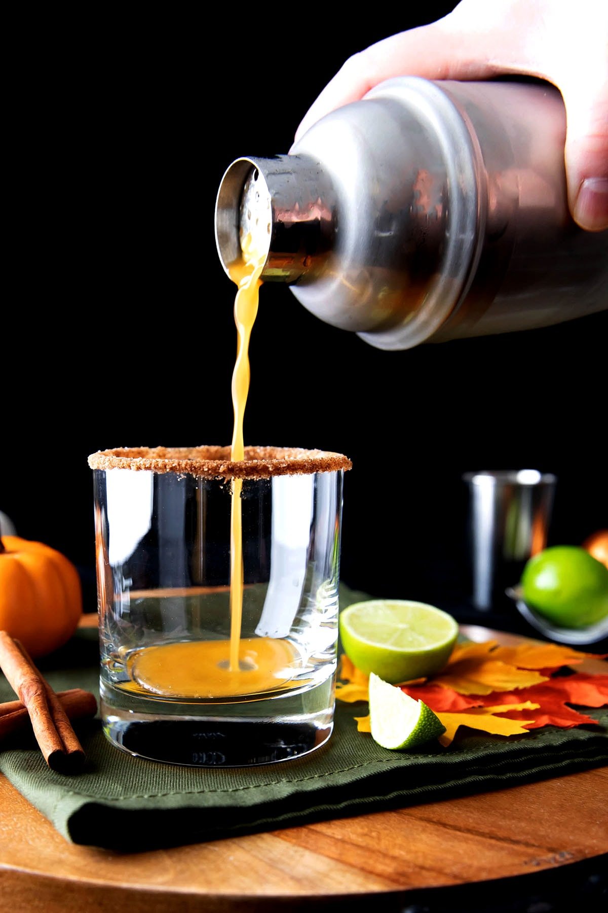 a hand pouring pumpkin spice margarita from a cocktail mixer into a glass