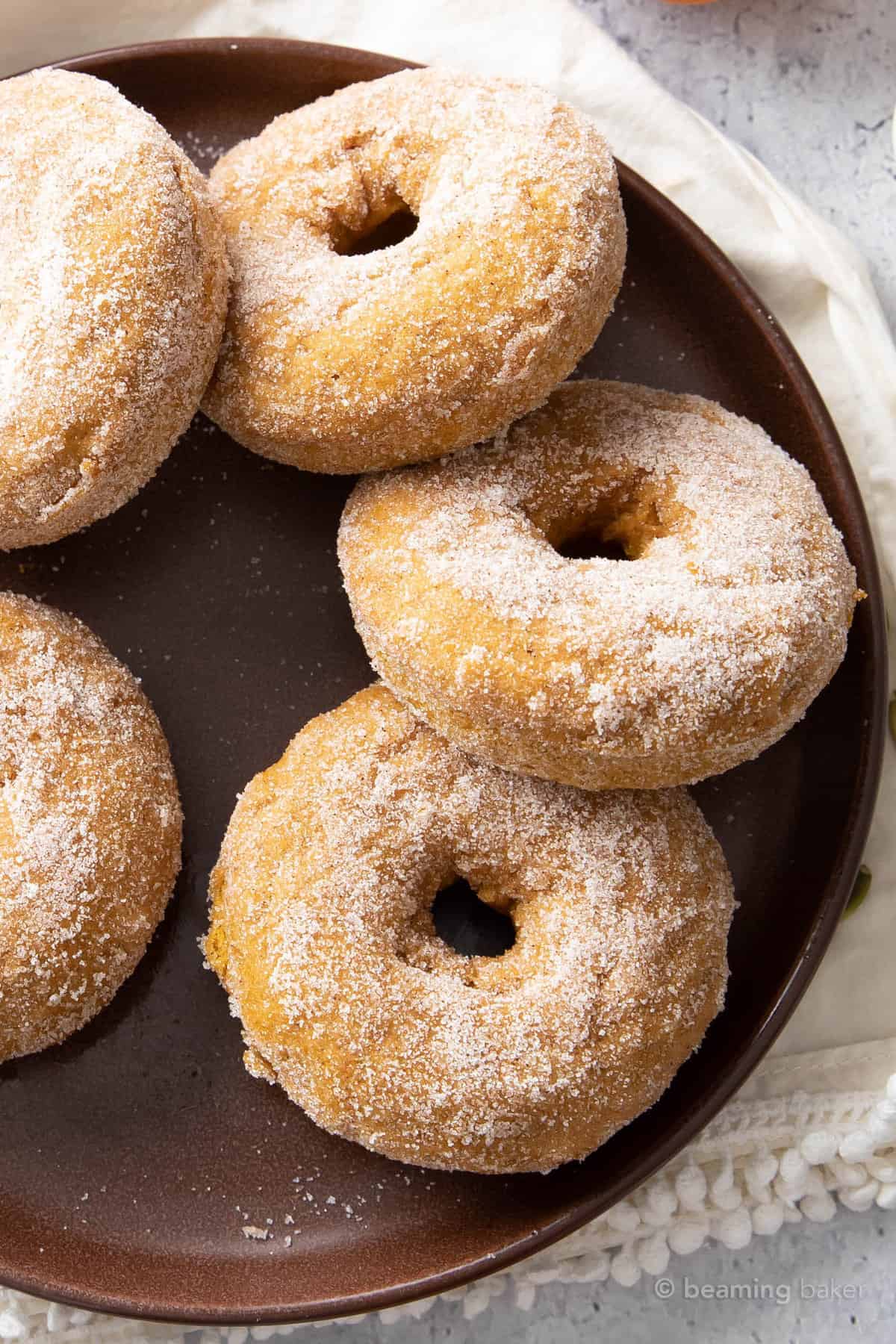 overhead photo of baked pumpkin donuts on a plate atop a kitchen cloth.