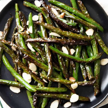 a square photo of blistered green beans on a plate with garnish