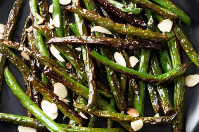 a square photo of blistered green beans on a plate with garnish