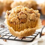 a square photo of cinnamon streusel muffins with the liner almost peeled off